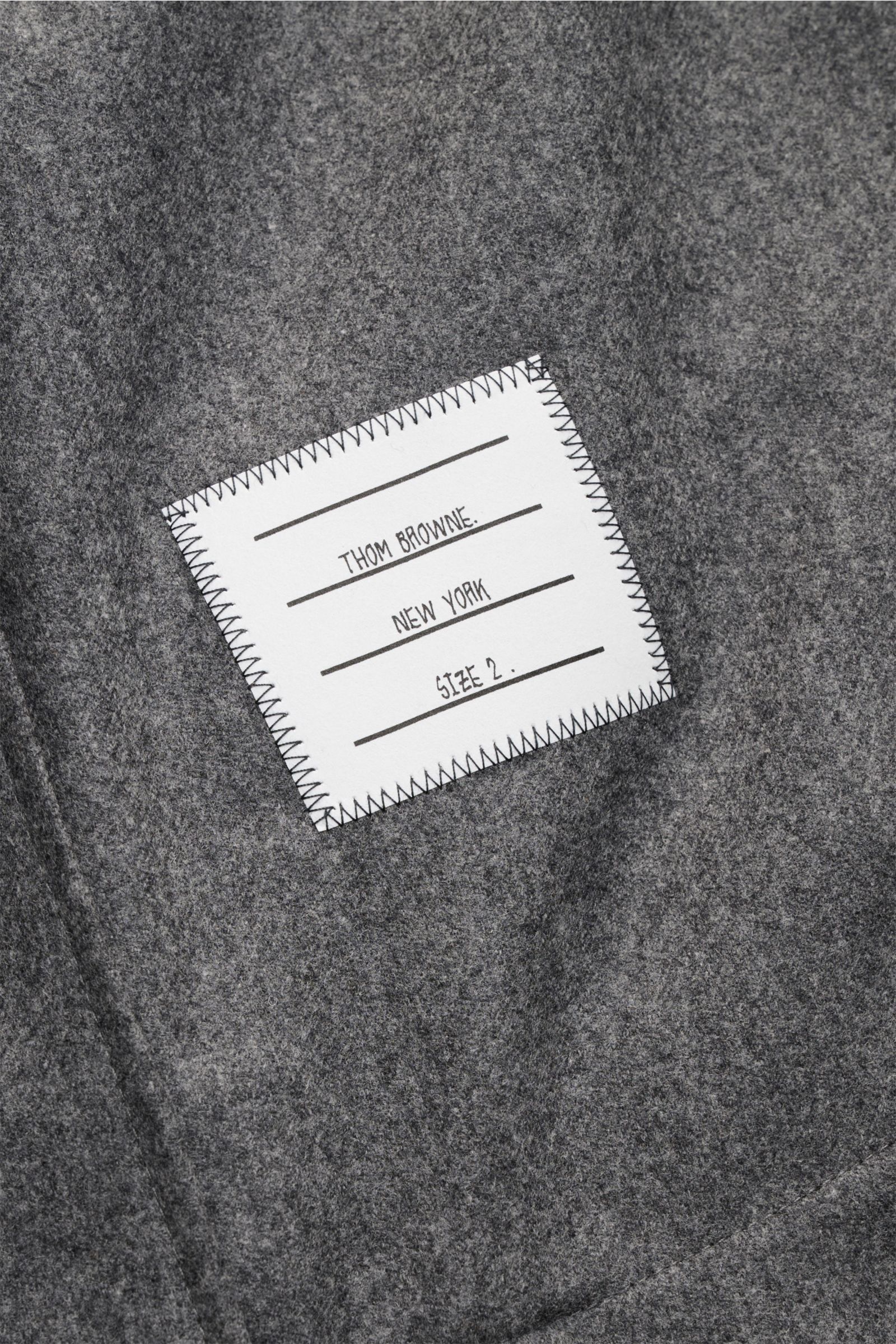 Alt-Tag (124 Zeichen): Nahaufnahme des Thom Browne Overshirt dunkelgrau meliert mit weichem Griff, tonalen Streifen am Ärmel und Brusttasche.