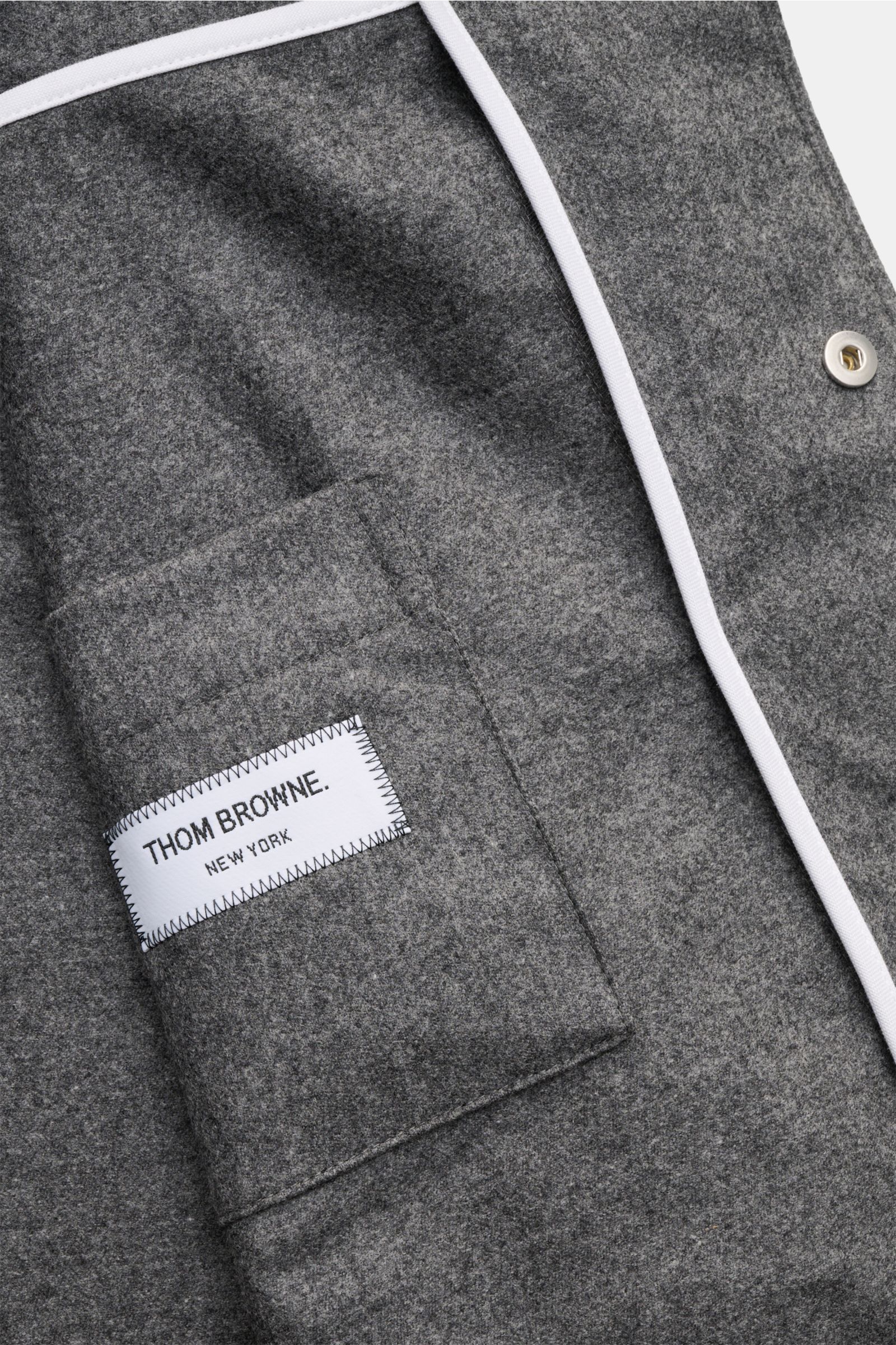 Nahaufnahme des Thom Browne Overshirts dunkelgrau meliert von oben, mit weichem Griff aus Wolle und Cashmere, tonalen Streifen am Ärmel, Brusttasche, schmalem Kragen und gerundetem Saum.