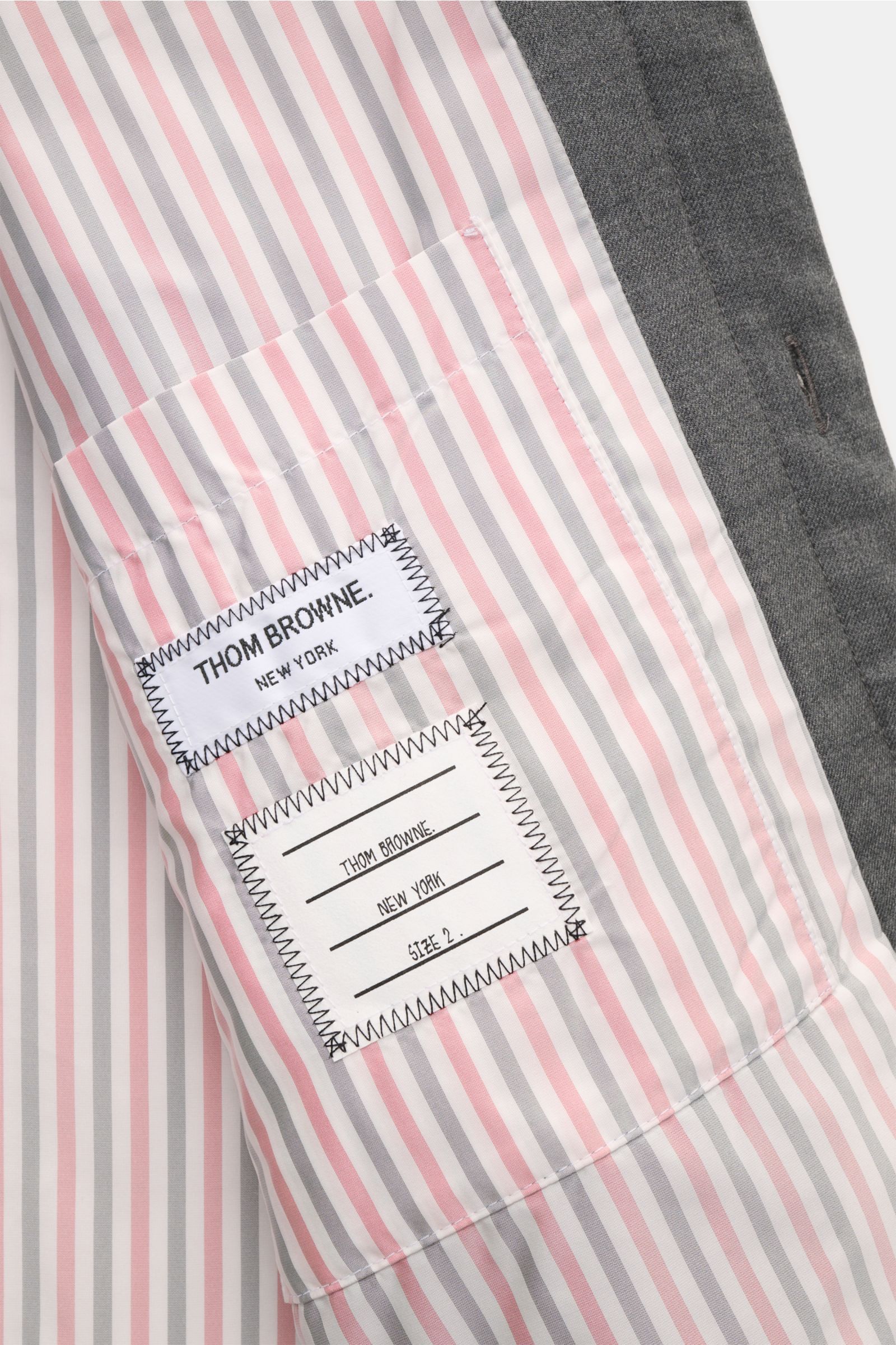 Close-up view of the interior of the Thom Browne Daunenjacke dunkelgrau meliert, showing striped pink, white, and gray lining with two stitched brand labels.

Preppy Jacke von THOM BROWNE: Gefertigt aus hochwertiger Wolle mit leichter Daunenfüllung und