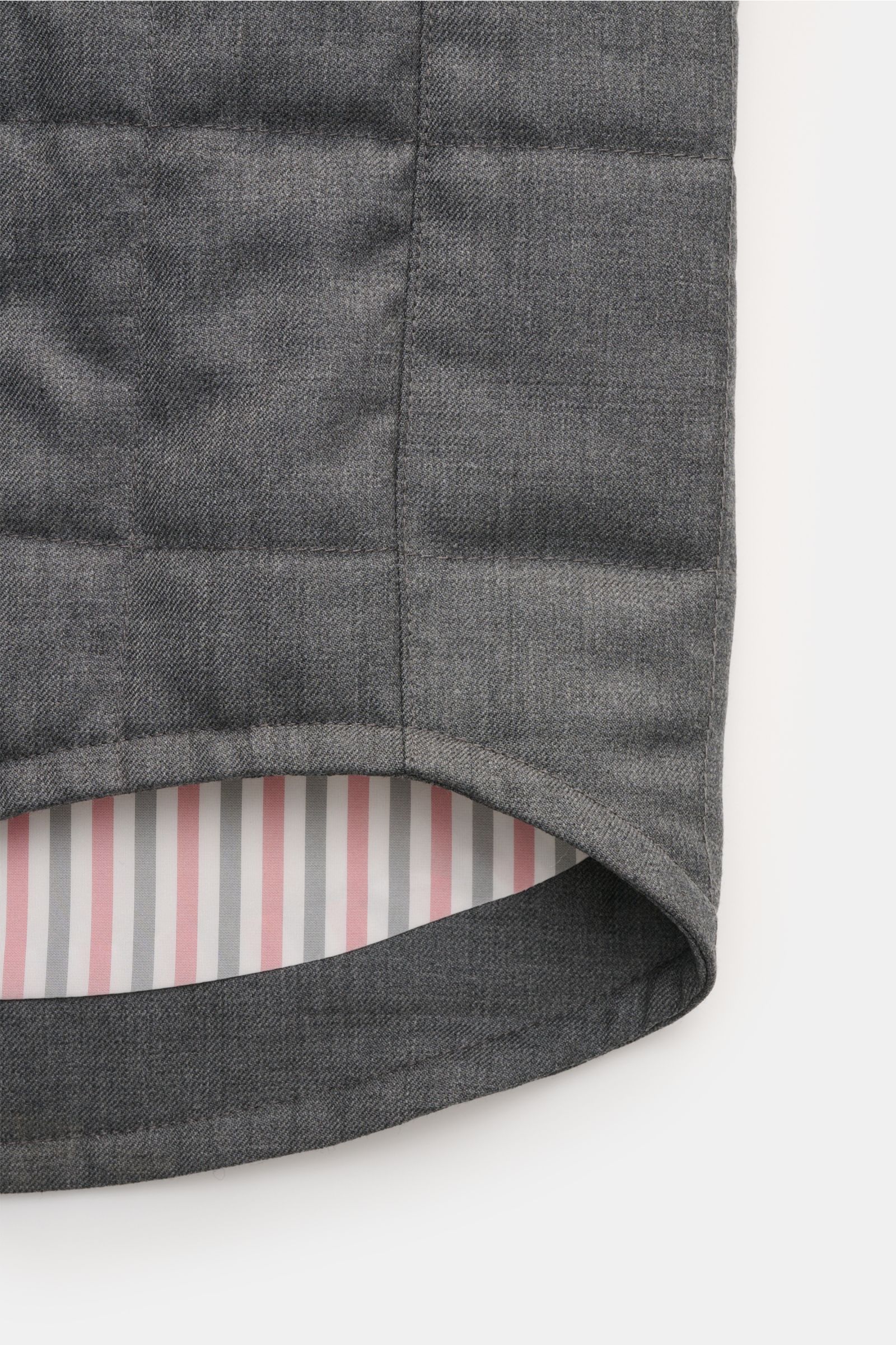 Close-up of the rounded hem and inner lining of the Thom Browne Daunenjacke dunkelgrau meliert, showing dark gray wool fabric with light down quilting from a side angle. Preppy Jacke von THOM BROWNE: Gefertigt aus hochwertiger Wolle mit leichter Daunen