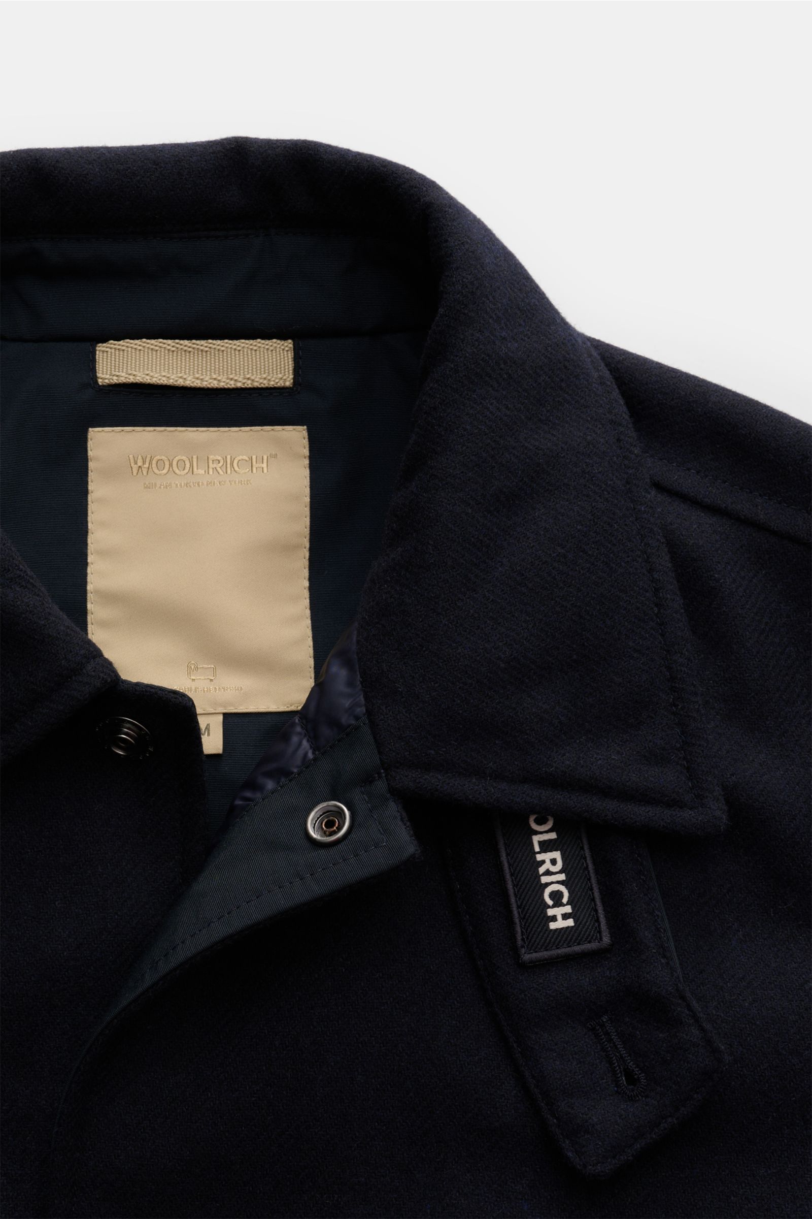 Close-up front view of Woolrich Daunenjacke navy showing collar, beige label, and snap button placket, made of Wolle und Microfaser, leichte Daunenfüllung, Slim Fit, Druckknopfleiste, variabler Kragen mit Knopfriegel, schräge Leistentaschen, Ärmelabschlüs