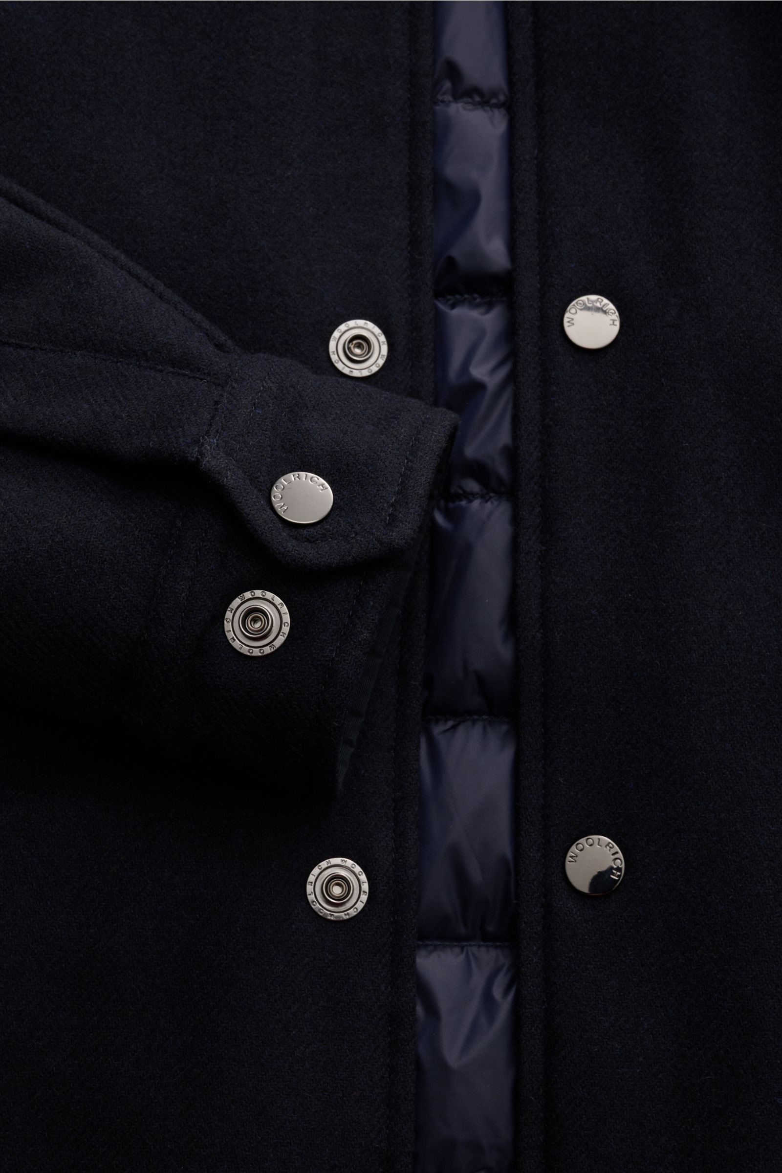 Close-up front view of Woolrich Daunenjacke navy showing snap button detail, sleeve cuff, and inner quilted lining, made of Wolle und Microfaser, leichte Daunenfüllung, Slim Fit, Druckknopfleiste, variabler Kragen mit Knopfriegel, schräge Leistentaschen, 