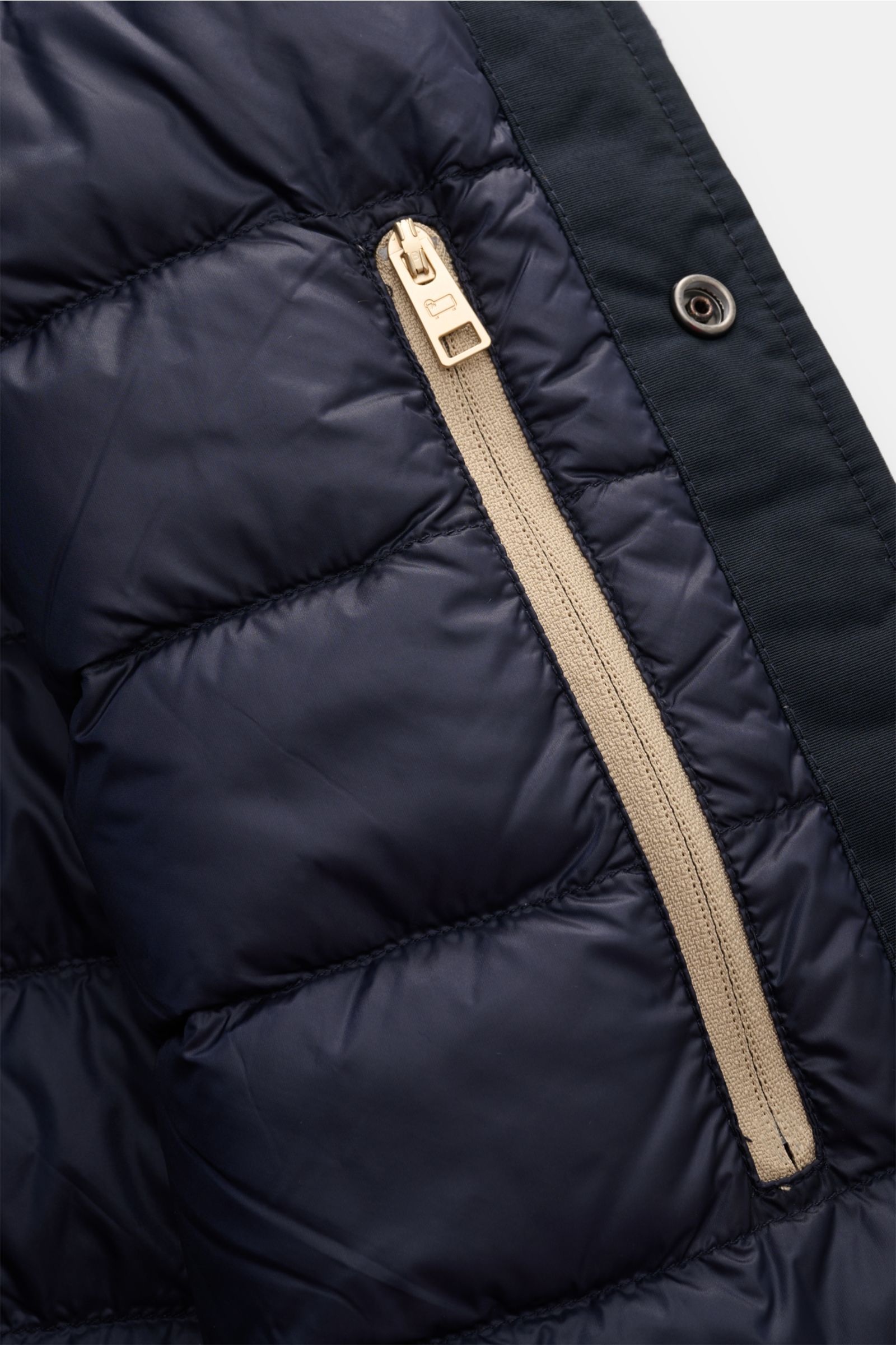 Close-up inner view of the Woolrich Daunenjacke navy showing a beige zipper on navy quilted fabric, featuring Wolle und Microfaser, leichte Daunenfüllung, Slim Fit, Druckknopfleiste, variabler Kragen mit Knopfriegel, schräge Leistentaschen, Ärmelabschlüss