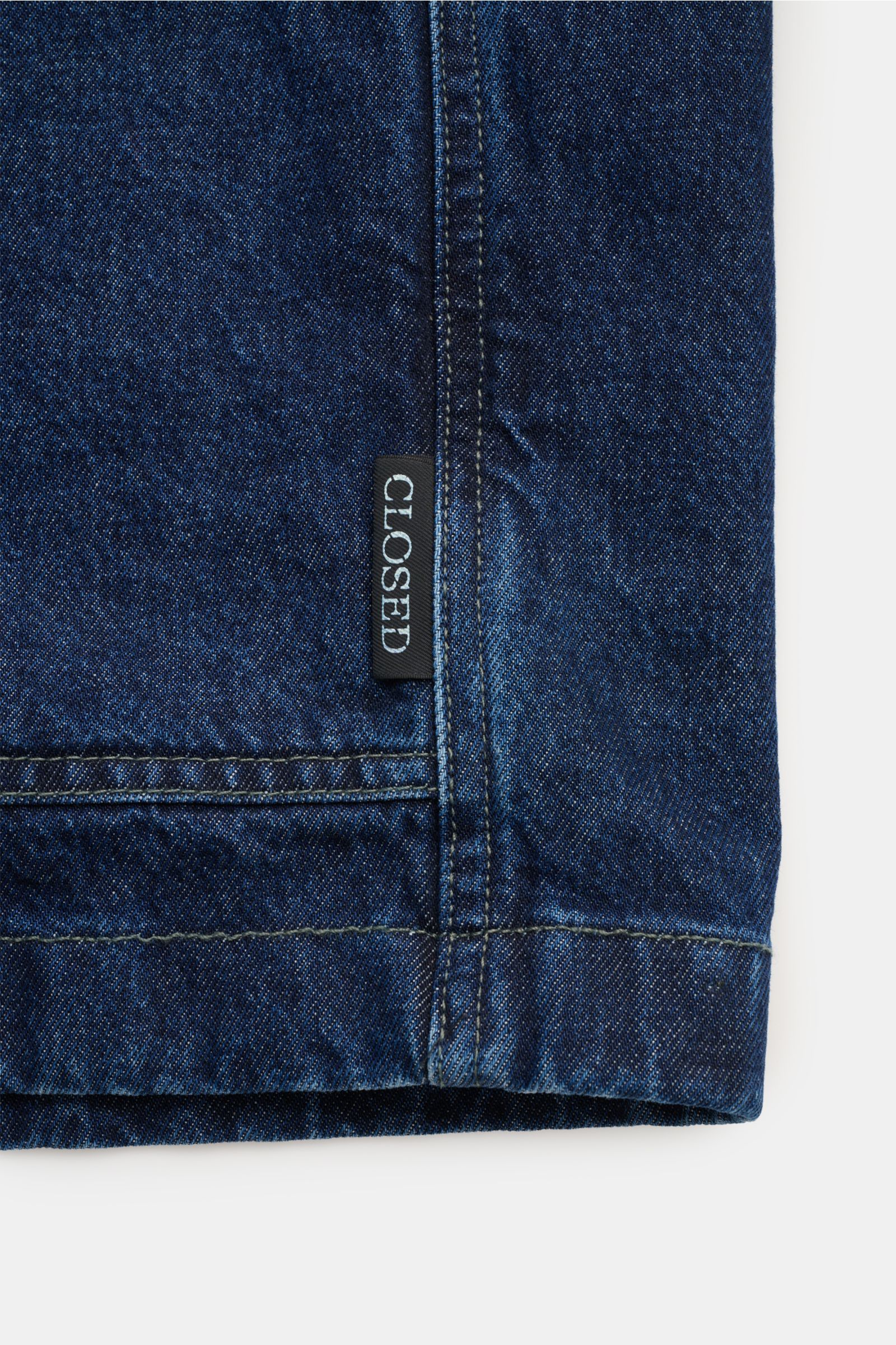 Close-up front bottom hem view of the Closed Denim-Overshirt 'Atelier Jacket' dunkelblau in deep indigo, made of pure cotton denim with a boxy, longer silhouette. Features include a regular fit, five-button placket, turn-down collar, patch chest pocket, l