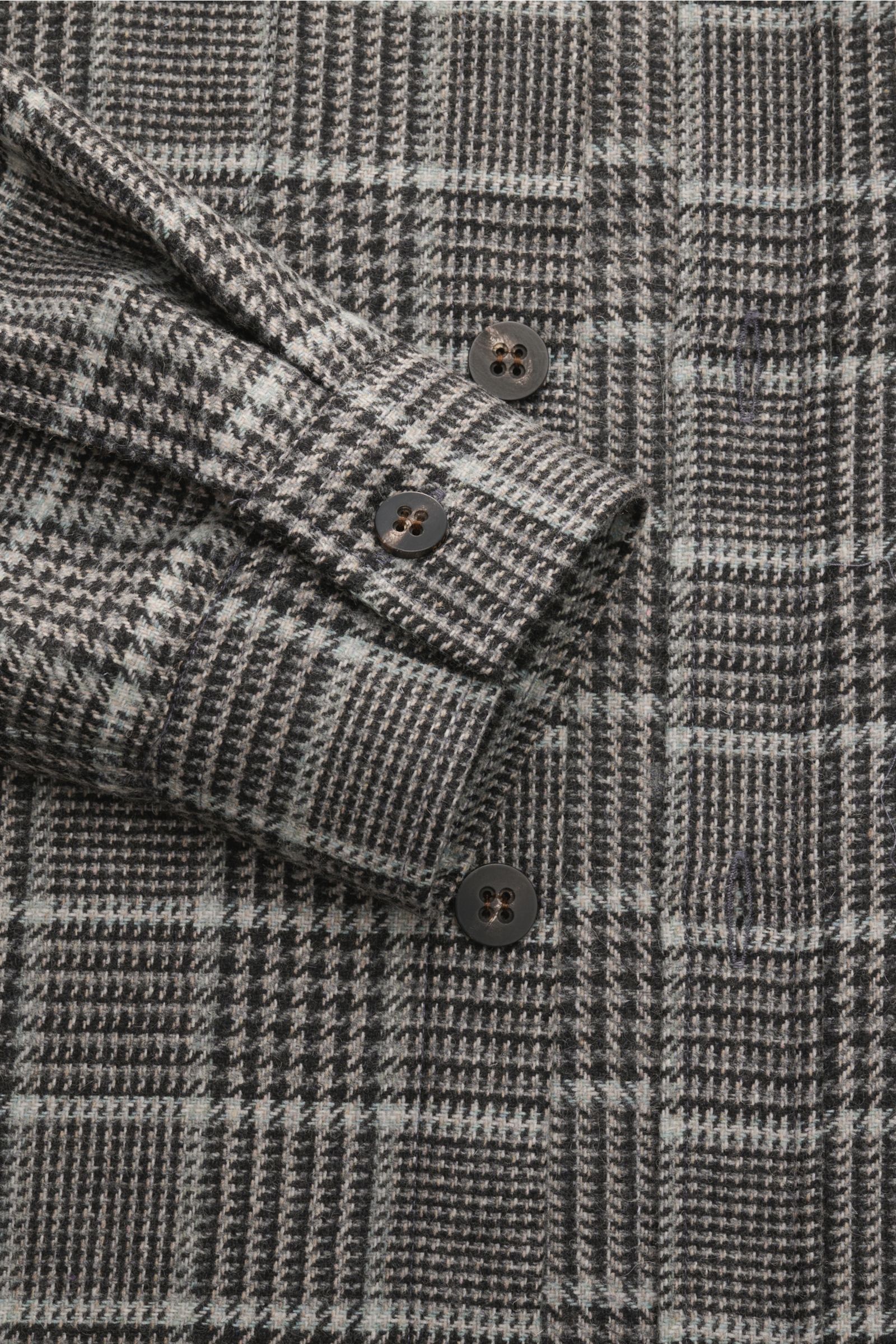 Close-up from above of the 04651/ A trip in a bag Overshirt schwarz/grau kariert showing its classic Glencheck pattern, soft wool-mix fabric, buttoned cuff, and chest pocket with flap. Das perfekte Styling-Piece für Ihre Freizeitgarderobe: Das karierte