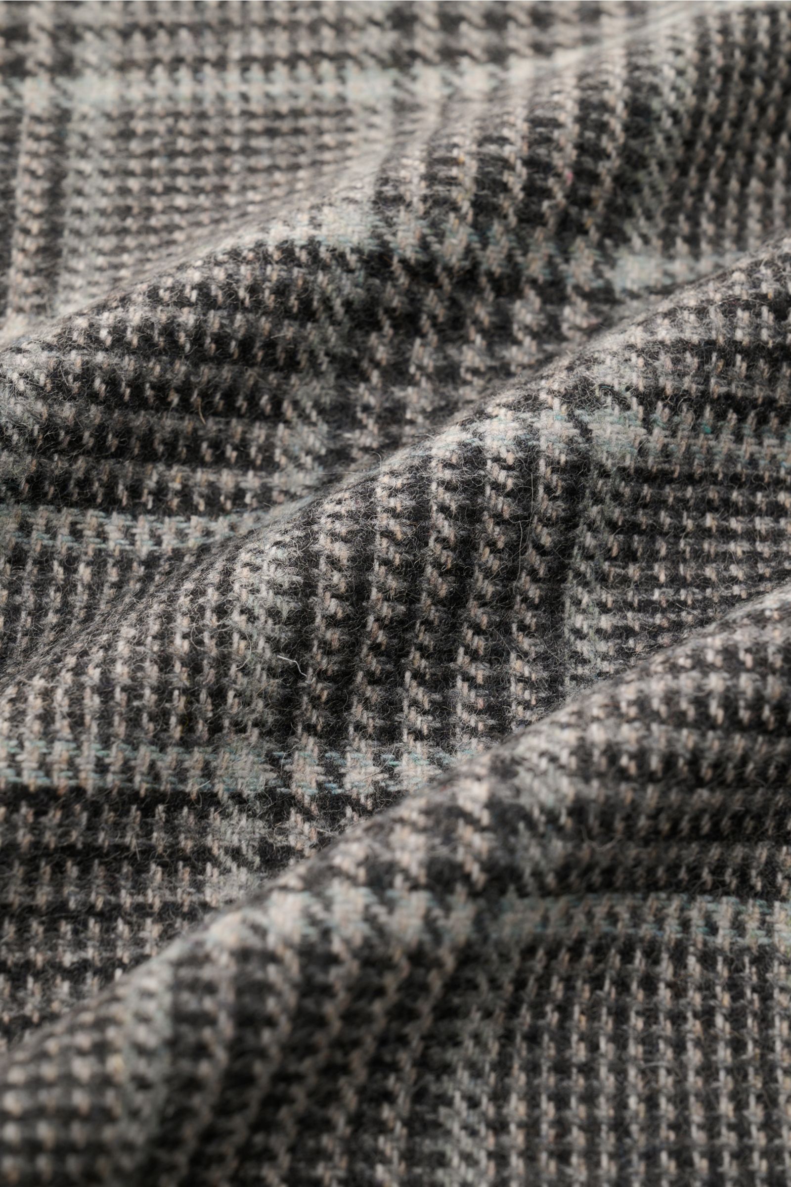 Close-up image of the fabric of the 04651/ A trip in a bag Overshirt schwarz/grau kariert, showing a soft, lightweight wool-mix with classic Glencheck pattern from a slightly angled top view. Das perfekte Styling-Piece für Ihre Freizeitgarderobe: Das k