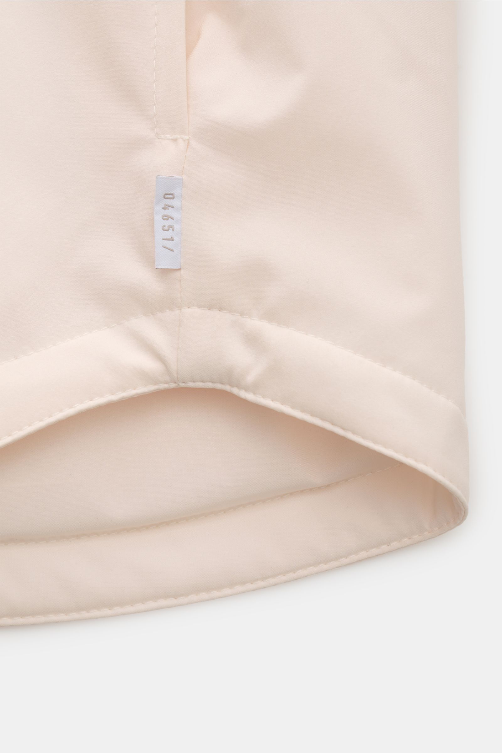 Close-up from below of the hem and side seam with label of the 04651/ A trip in a bag Overshirt 'Travel' creme, featuring smooth technical microfiber, lightweight padding, and precise stitching.