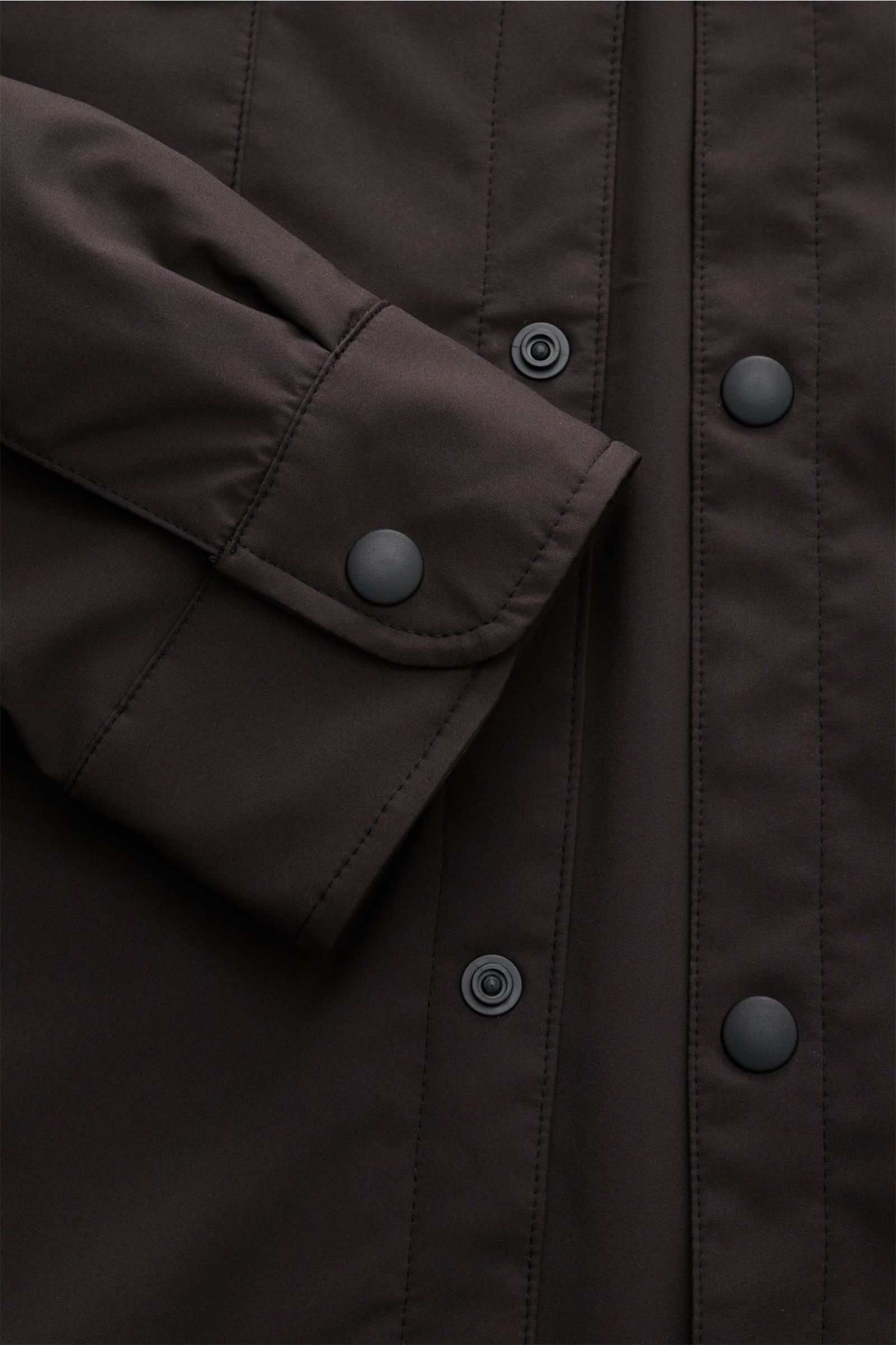 Dunkelbraunes 04651/ A trip in a bag Overshirt 'Travel' im Nahaufnahme von Ärmel und Druckknopfleiste, wind- und wasserabweisend.