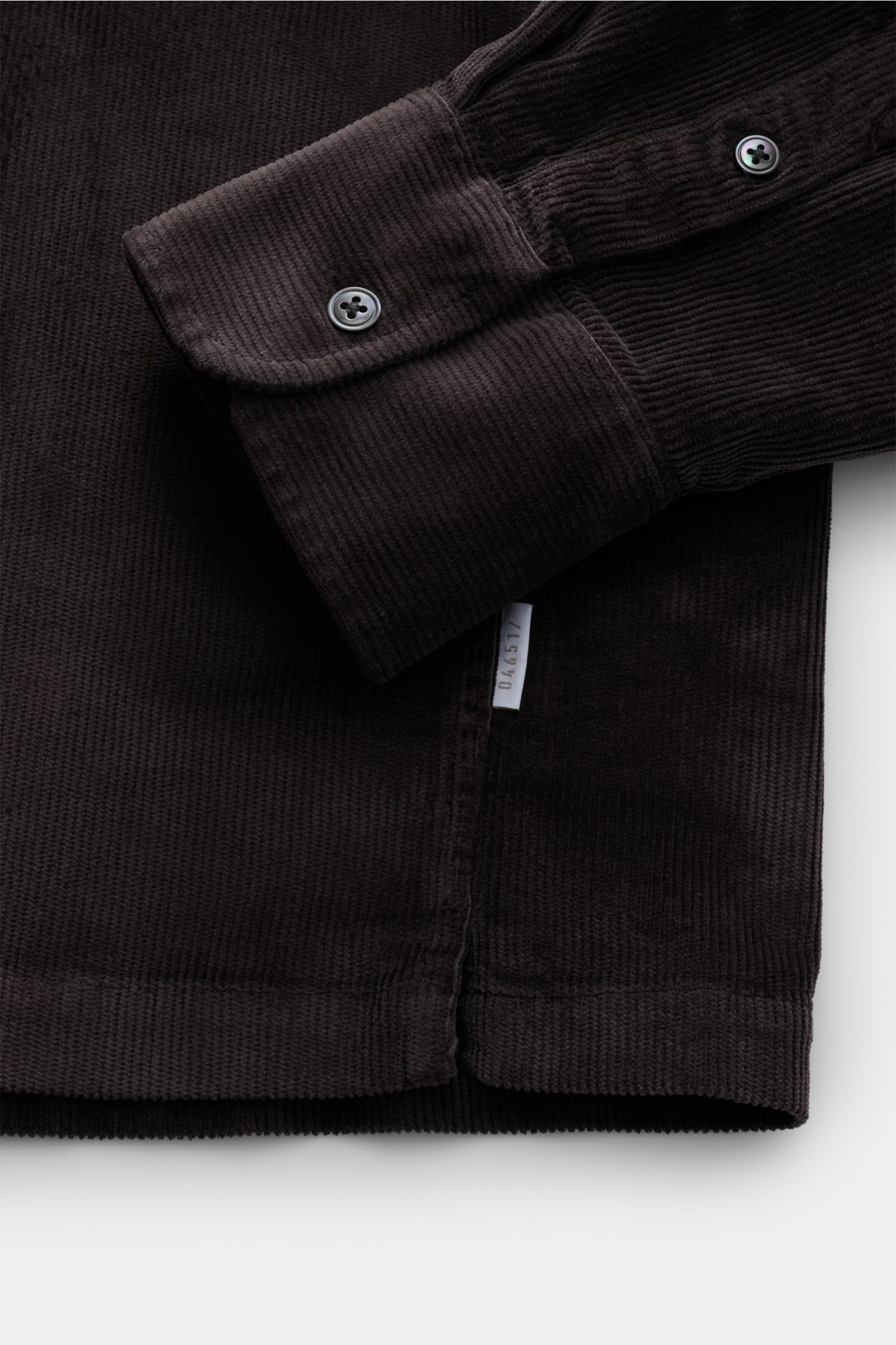 Nahaufnahme des geraden Saumverlaufs und der klassischen Sportmanschette mit Knopf eines dunkelbraunen 04651/ A trip in a bag Popover-Cordhemd Grandad-Kragen aus weichem Baumwolle-Modal-Mix.