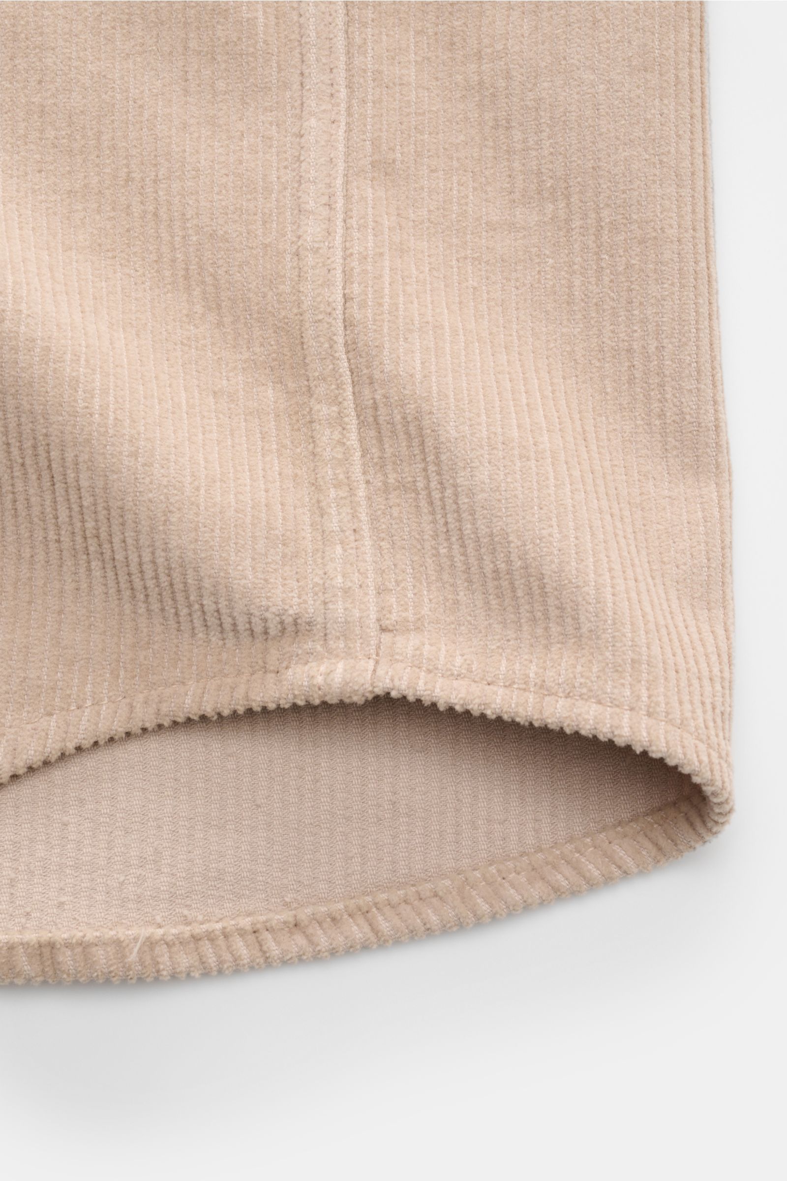 Close-up of the beige Ace Denim Cord-Overshirt hem, showing the soft pure cotton corduroy fabric, curved edge, and detailed stitching from a front angle.