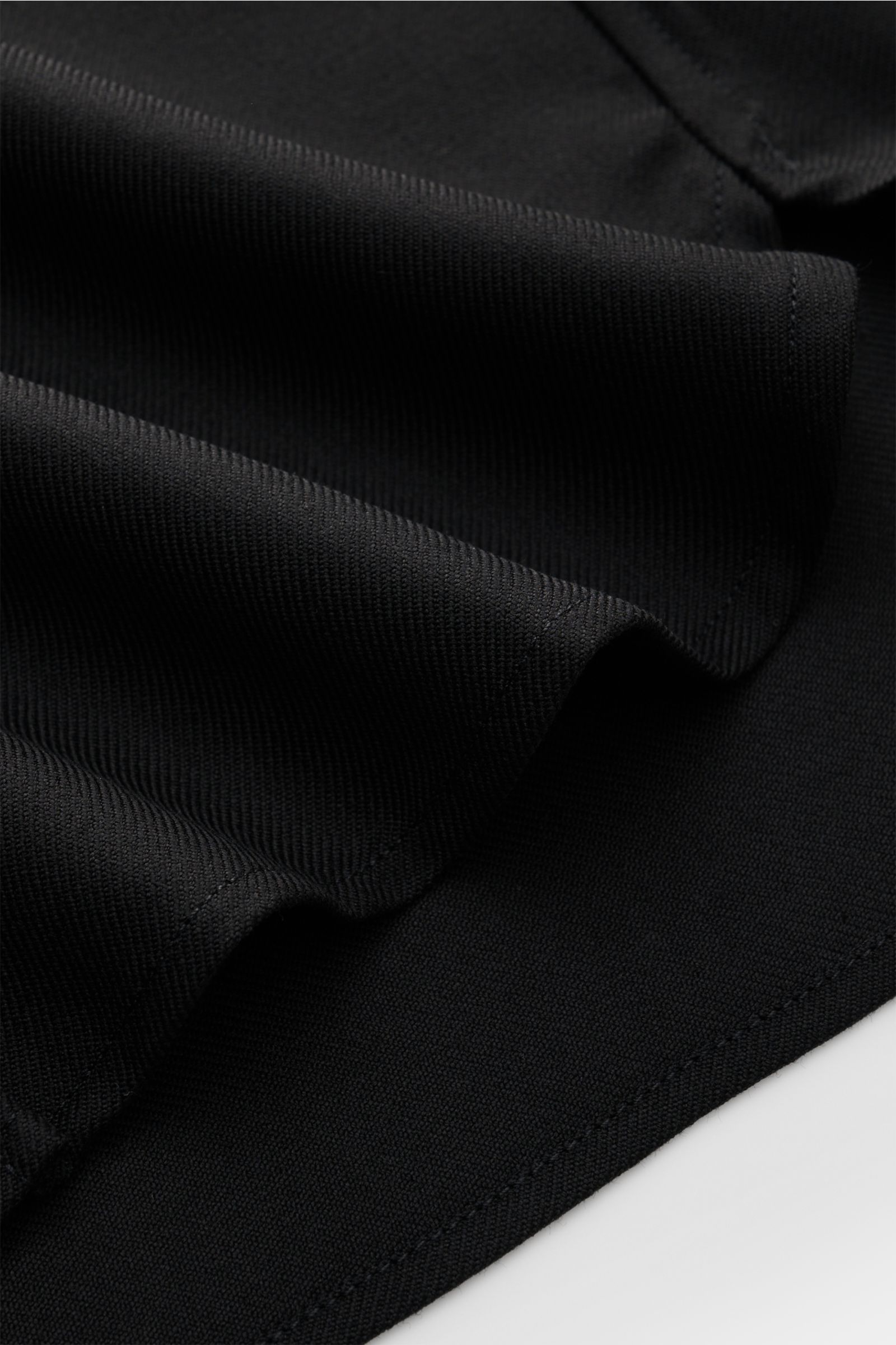 A close-up angled view of the fabric and stitching details of the A.P.C. Overshirt schwarz, featuring a minimalist essential design with a wool and microfiber blend, lightly textured quality, regular fit, seven-button placket, turn-down collar, patch ches