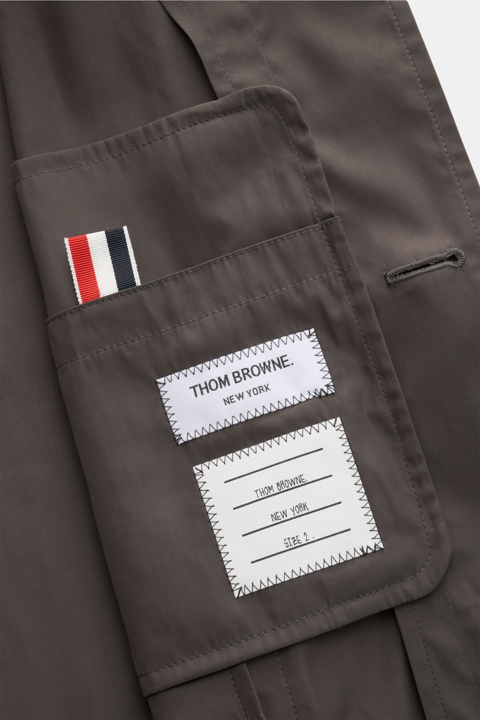 Nahaufnahme des Innentaschenbereichs vom Thom Browne Overshirt anthrazit aus hochwertiger Microfaser mit glattem Griff und Label-Details.