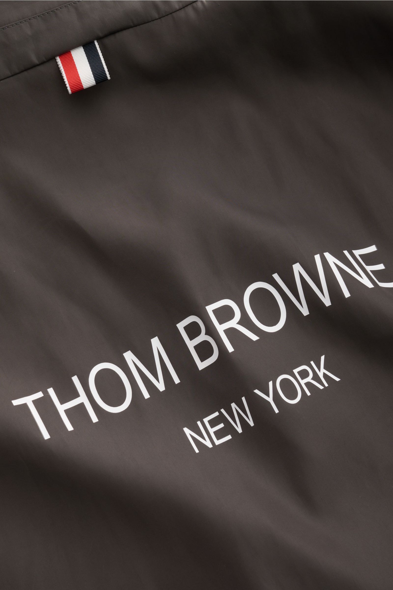 Thom Browne Overshirt anthrazit, Detailaufnahme von hinten mit Logo-Print, hochwertiger Microfaser, glattem Griff und rotem Webband.