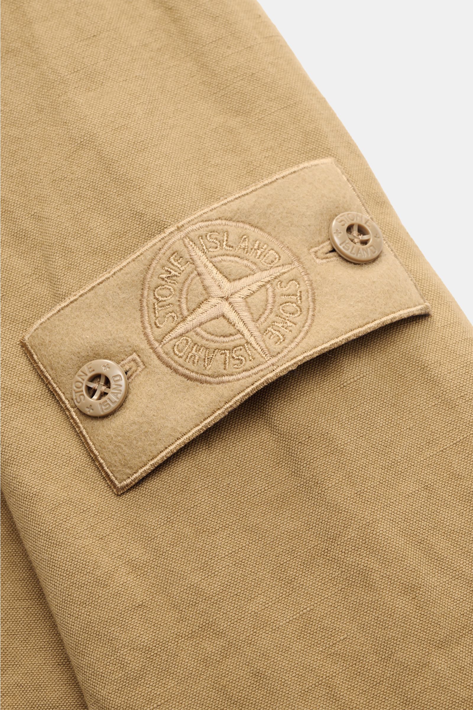 Close-up view of the Stone Island Overshirt 'Ghost' khaki sleeve showing the embroidered compass badge with buttoned cuff, made from a cotton-linen mix.

Zeitloses Layering-Piece: Das Overshirt aus der 'Ghost' Capsule von STONE ISLAND ergänzt lässige F