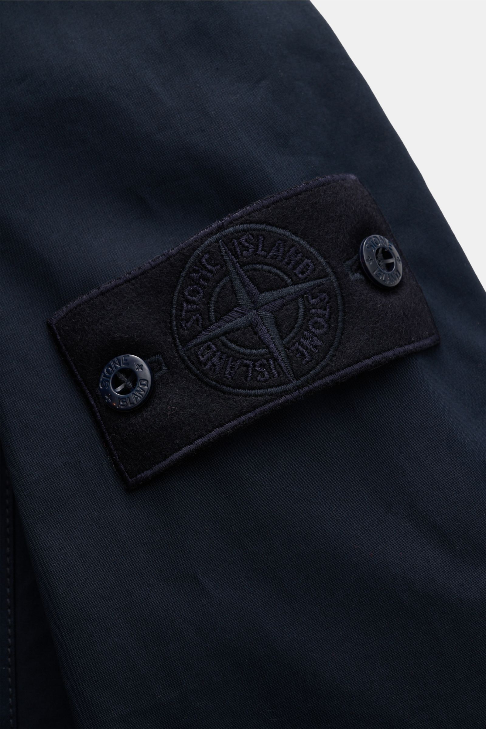 Close-up of the tonal Stone Island badge on the sleeve of the Stone Island Overshirt 'Ghost Piece' navy, showing navy cotton canvas fabric and button details from a front-side perspective. Funktion trifft Komfort: Das STONE ISLAND Overshirt aus der 'Ghost