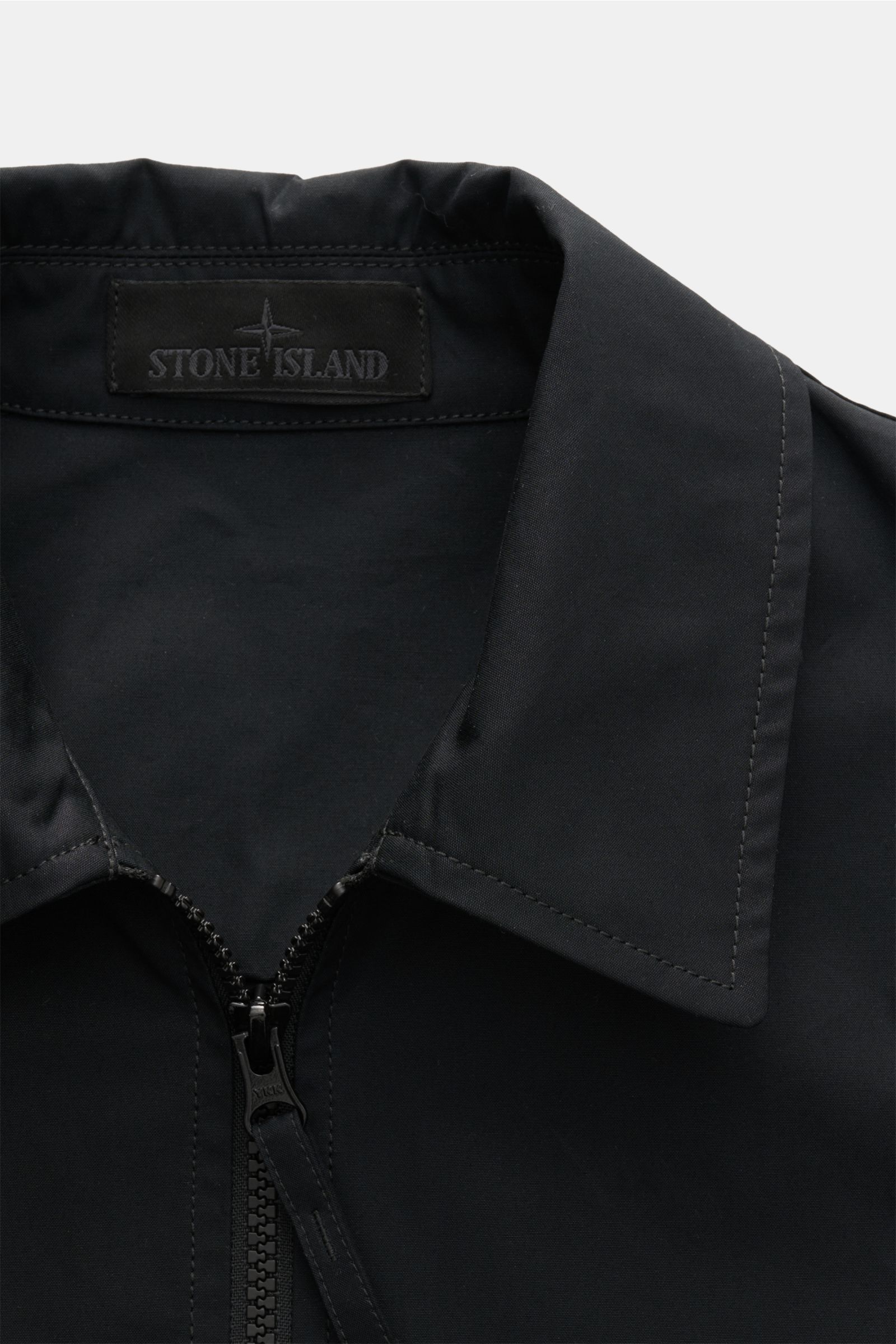 Close-up front view of the Stone Island Overshirt 'Ghost Piece' black, showing the turn-down collar, robust two-way zip, and tonal Stone Island badge inside collar. Function meets comfort: this overshirt from the 'Ghost' capsule is made of uniquely comfor