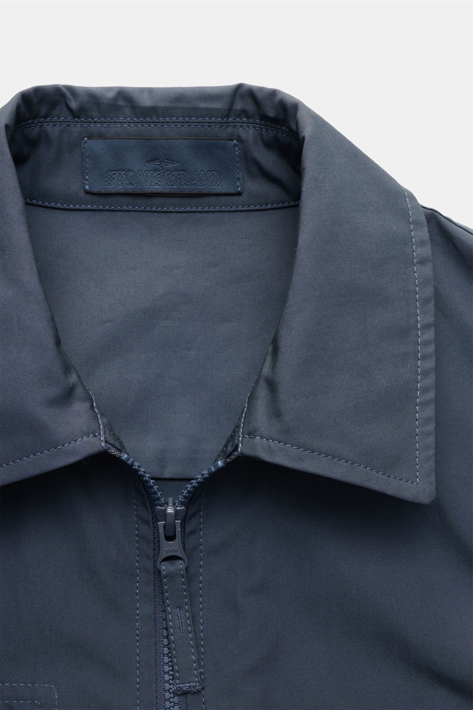 Stone Island Overshirt 'Ghost Piece' graublau, Nahaufnahme von Umlegekragen, robustem Zwei-Wege-Reißverschluss und glattem Baumwollcanvas.