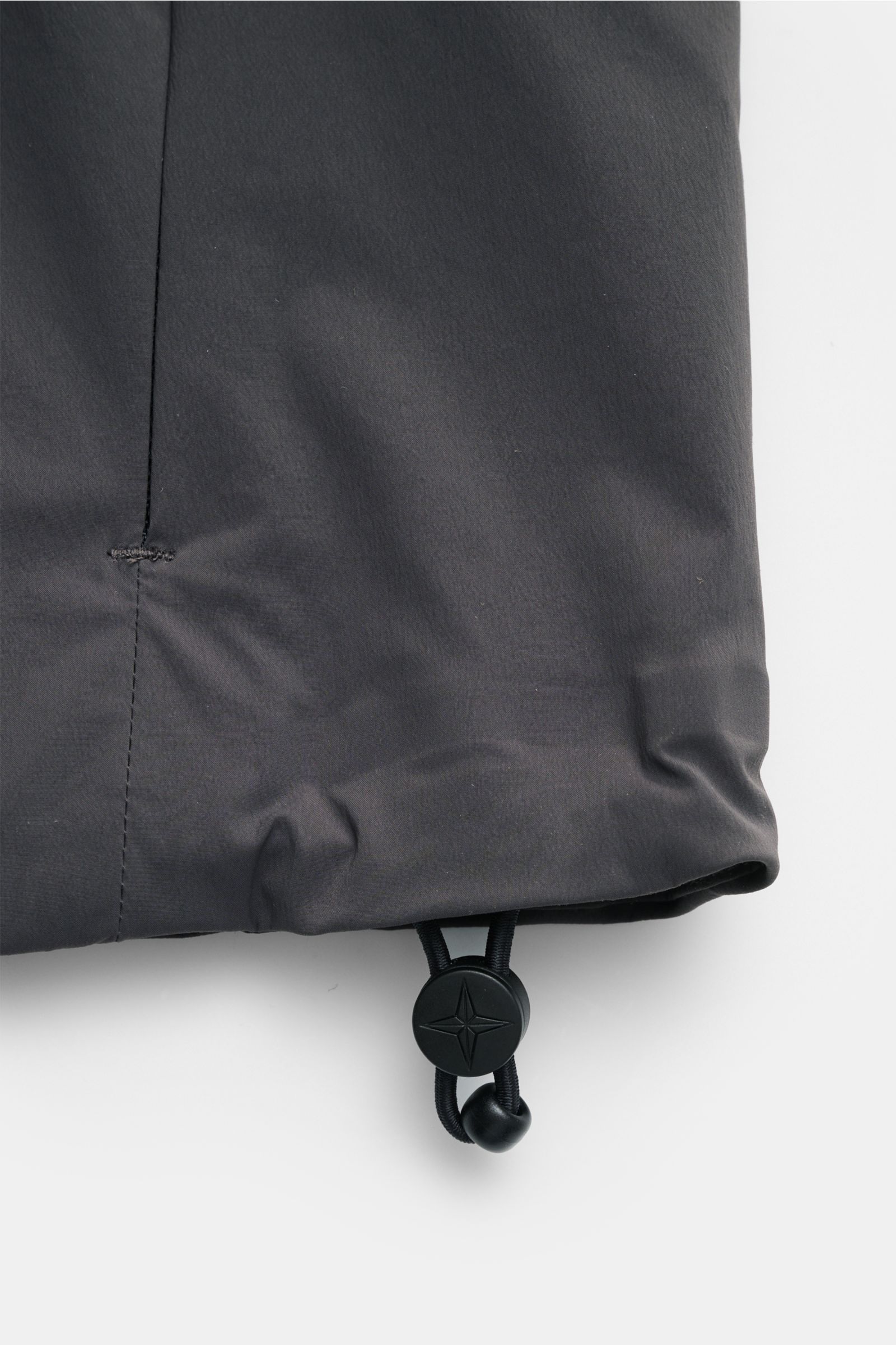 Nahaufnahme der regulierbaren Saumweite der Stone Island Jacke 'Stellina' dunkelgrau aus glatter Microfaser mit elastischem Kordelzug, Detail von unten fotografiert.