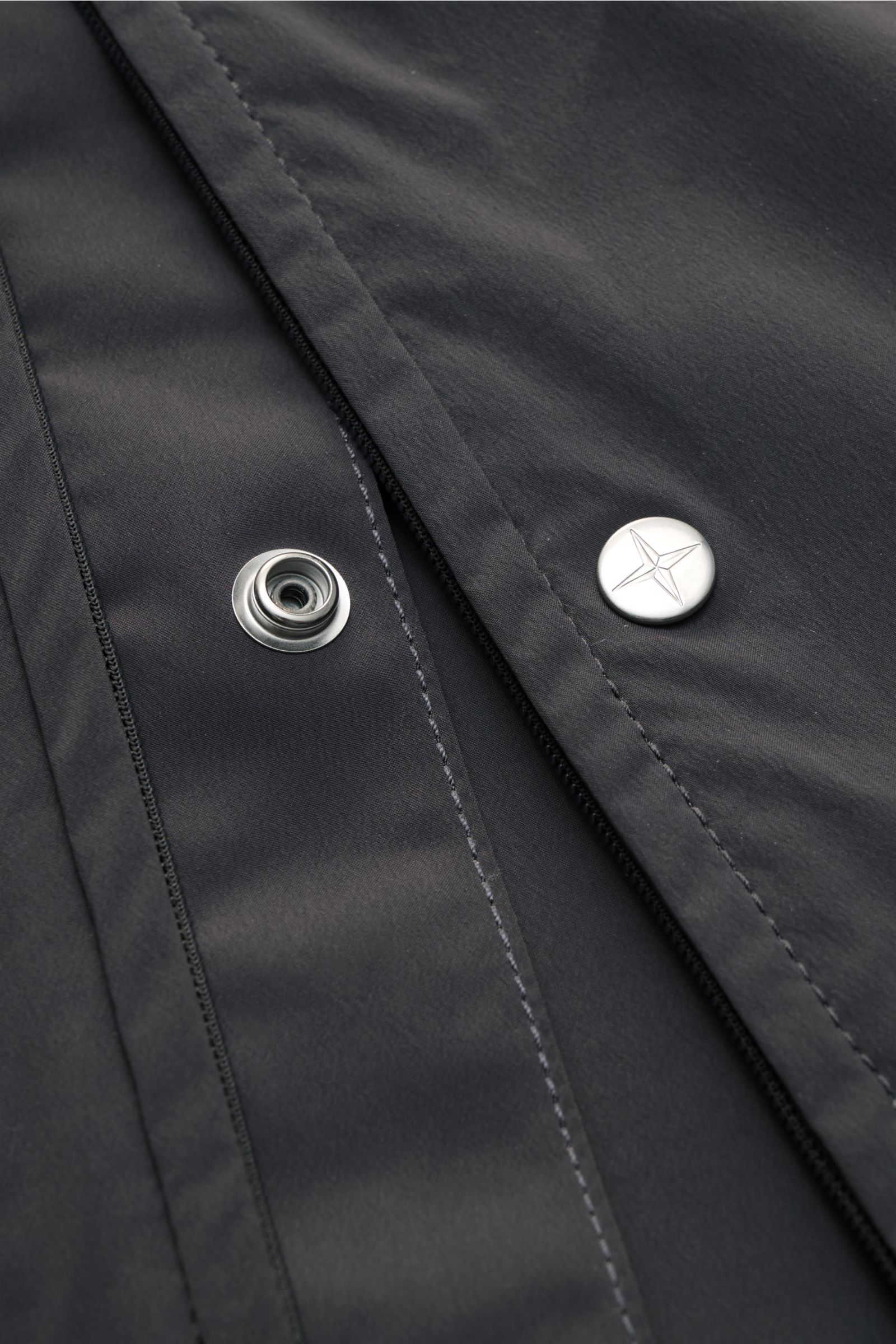 Nahaufnahme der Stone Island Jacke 'Stellina' dunkelgrau, Front mit silbernem Druckknopf und hochwertiger Microfaser.