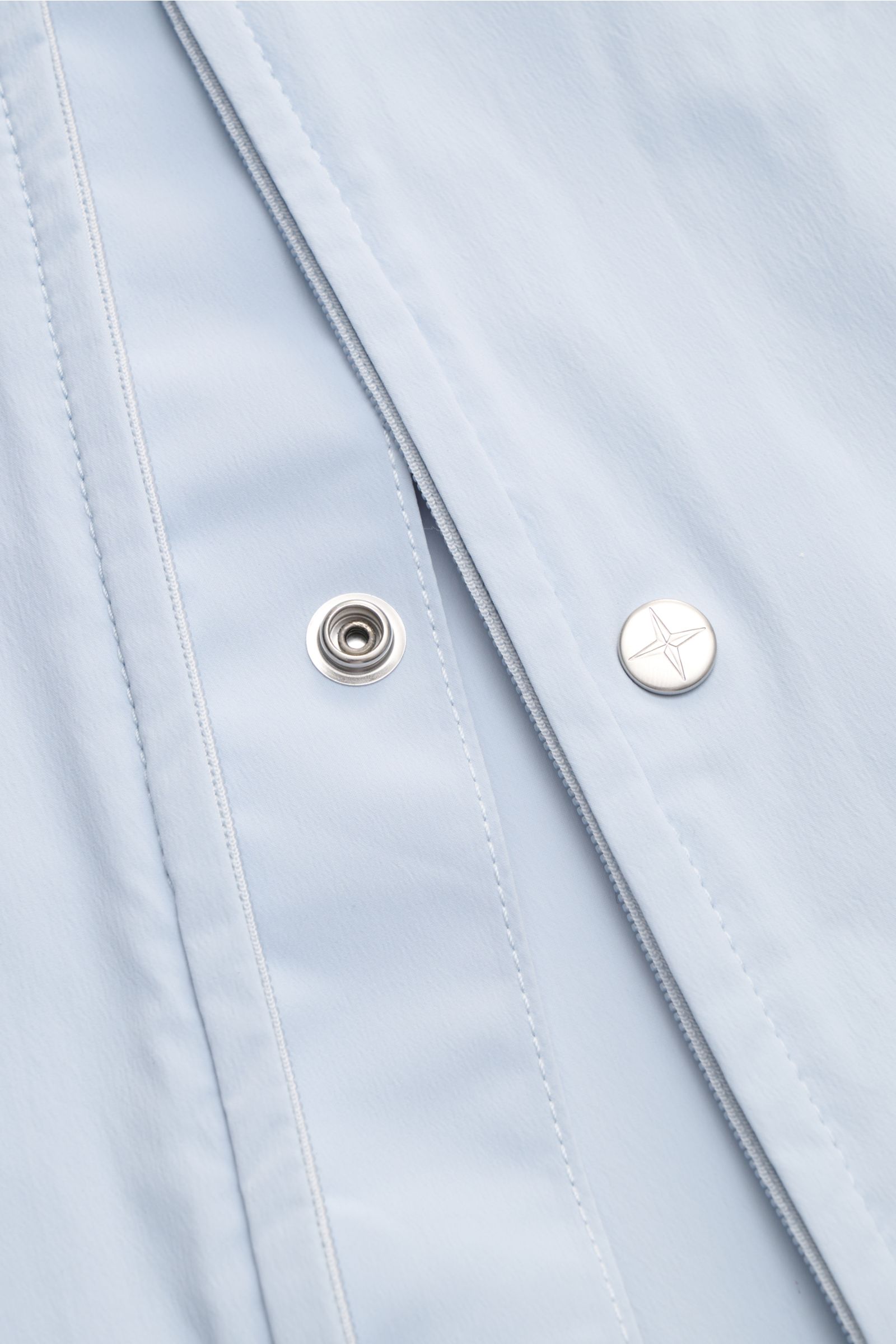 Close-up front view of Stone Island Jacke 'Stellina' hellblau in light blue microfiber with smooth texture, two-way zipper, snap button, and detailed stitching, showcasing urbane Frühlingslooks features like zipper front pockets, elastic cuffs, and adjust