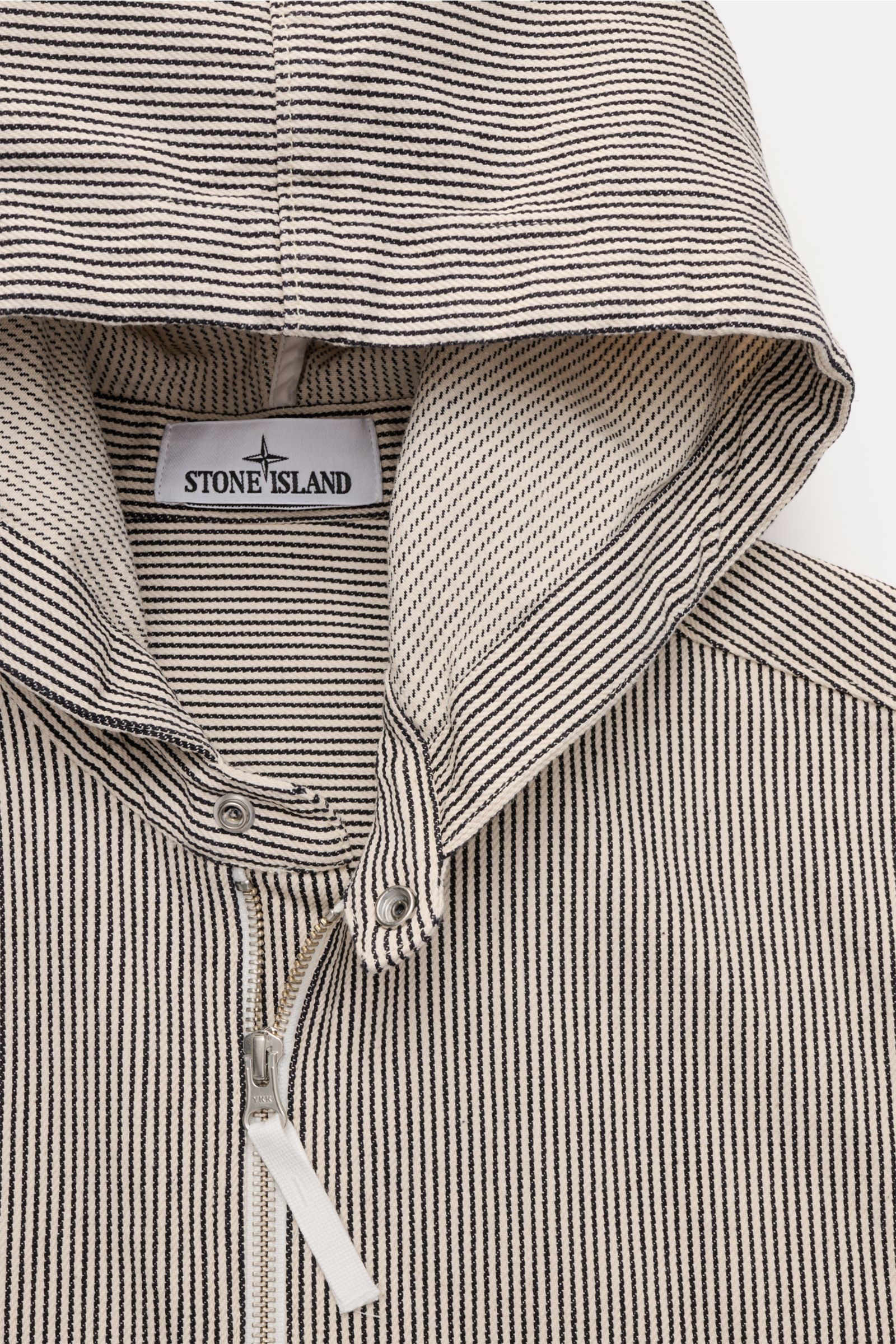 Nahaufnahme der Kapuze und des oberen Frontbereichs der Stone Island Jacke 'Marina' navy/beige gestreift aus reiner Baumwolle mit Streifenmuster, robustem Zwei-Wege-Reißverschluss und Tunnelzug-Kapuze, fotografiert von vorne oben.