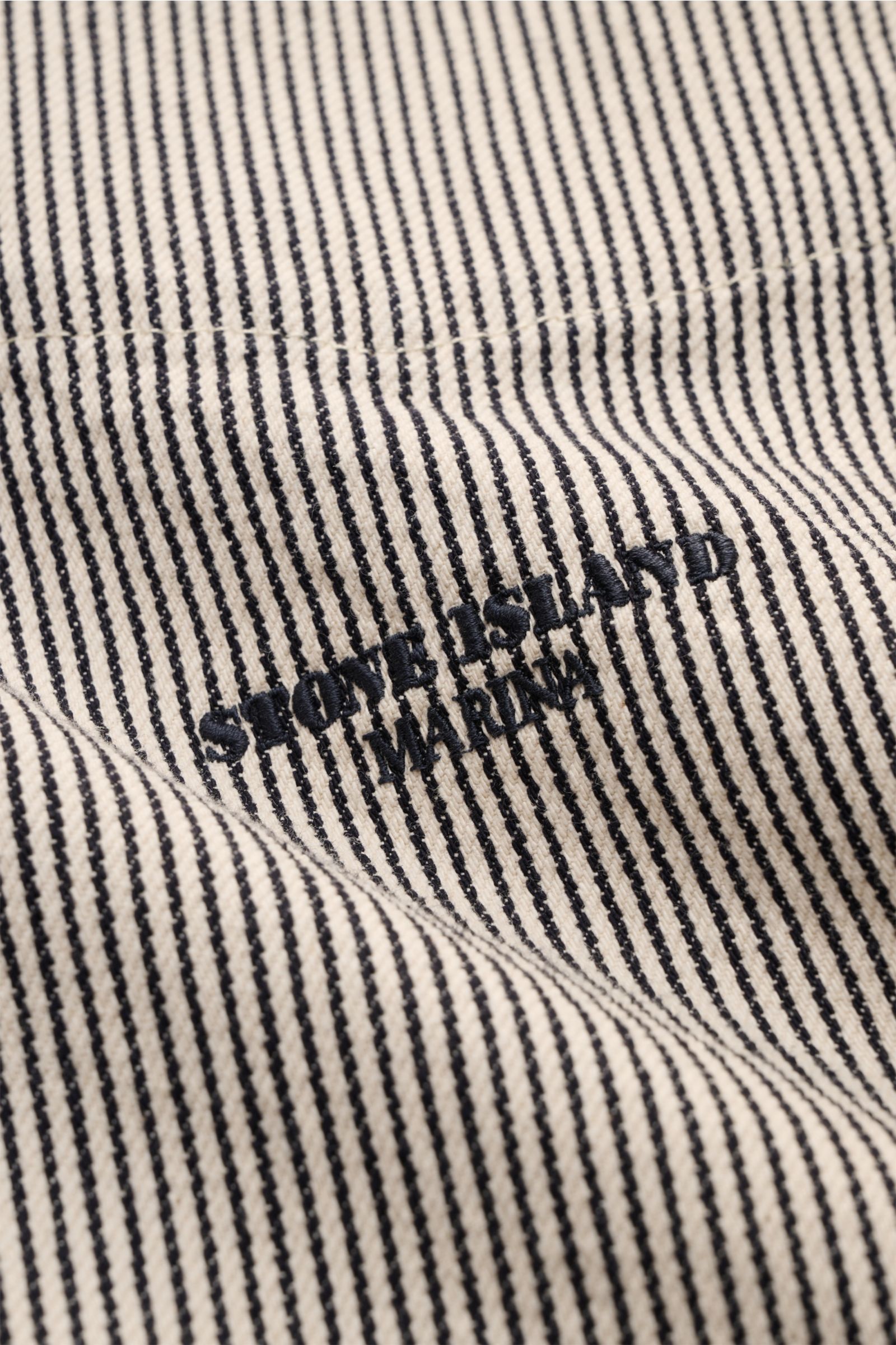Close-up front view of Stone Island Jacke 'Marina' navy/beige gestreift showing navy striped pure cotton fabric with MARINA stitching, part of light maritime outerwear with relaxed silhouette, robust two-way zipper, hood with drawstring, chest pocket, sna