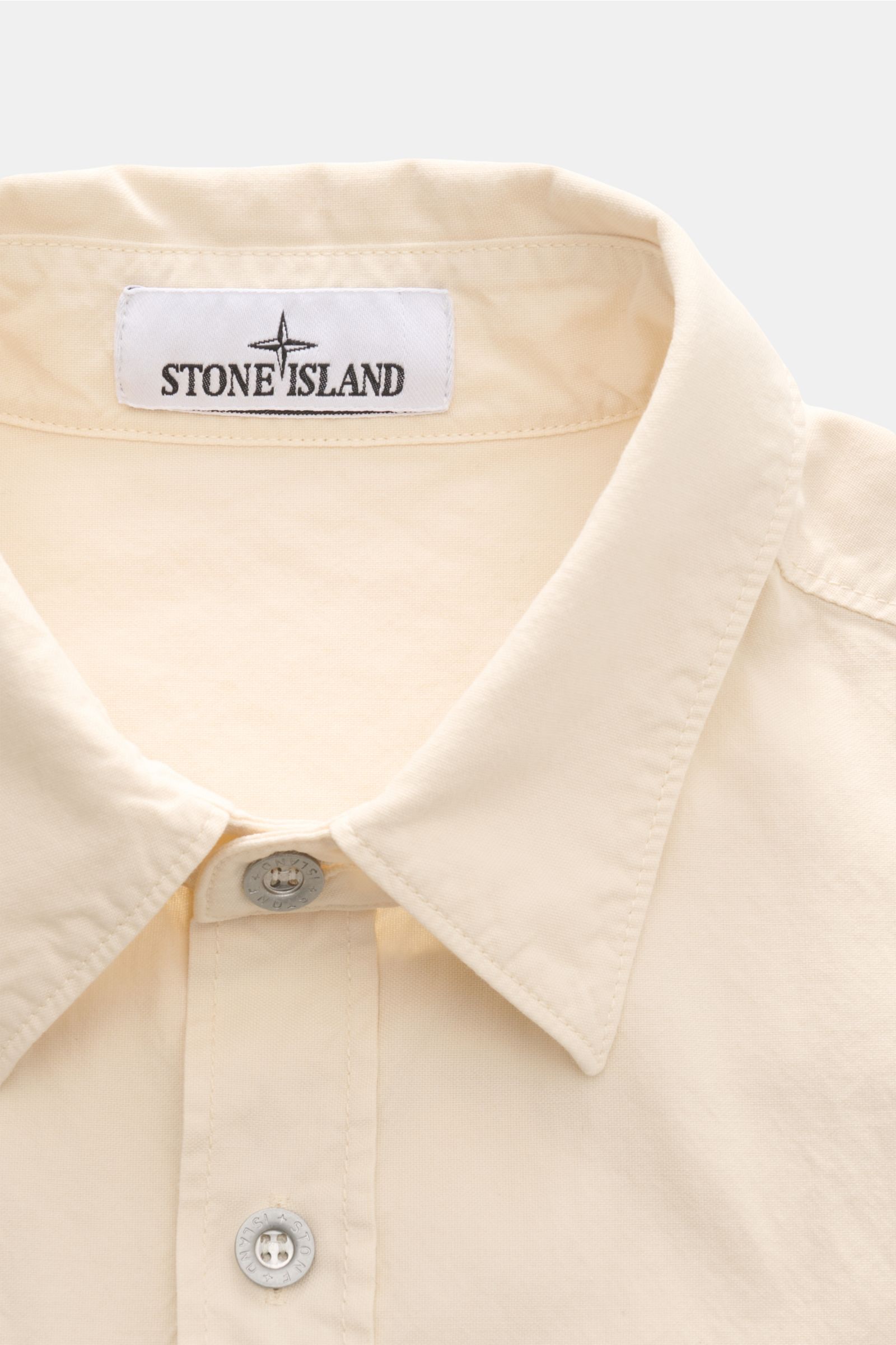 Stone Island Overshirt 'Marina' creme shown from a close-up front perspective highlighting the collar, two buttons, and Stone Island label. Maritimes Layering-Piece: Das Overshirt aus der STONE ISLAND 'Marina' Capsule Collection verbindet leichtes Panama-
