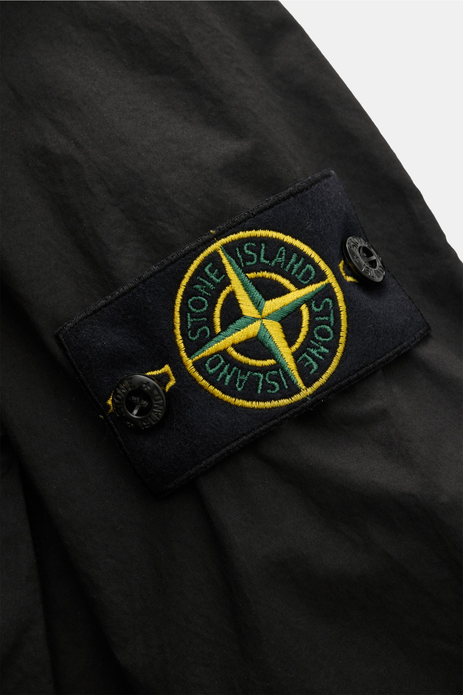Close-up front view of the Stone Island Overshirt schwarz showing the black fabric and the iconic compass badge on the upper arm, made of elastic cotton with a soft touch, slim fit, concealed snap button placket, turn-down collar, patch chest pocket, and 
