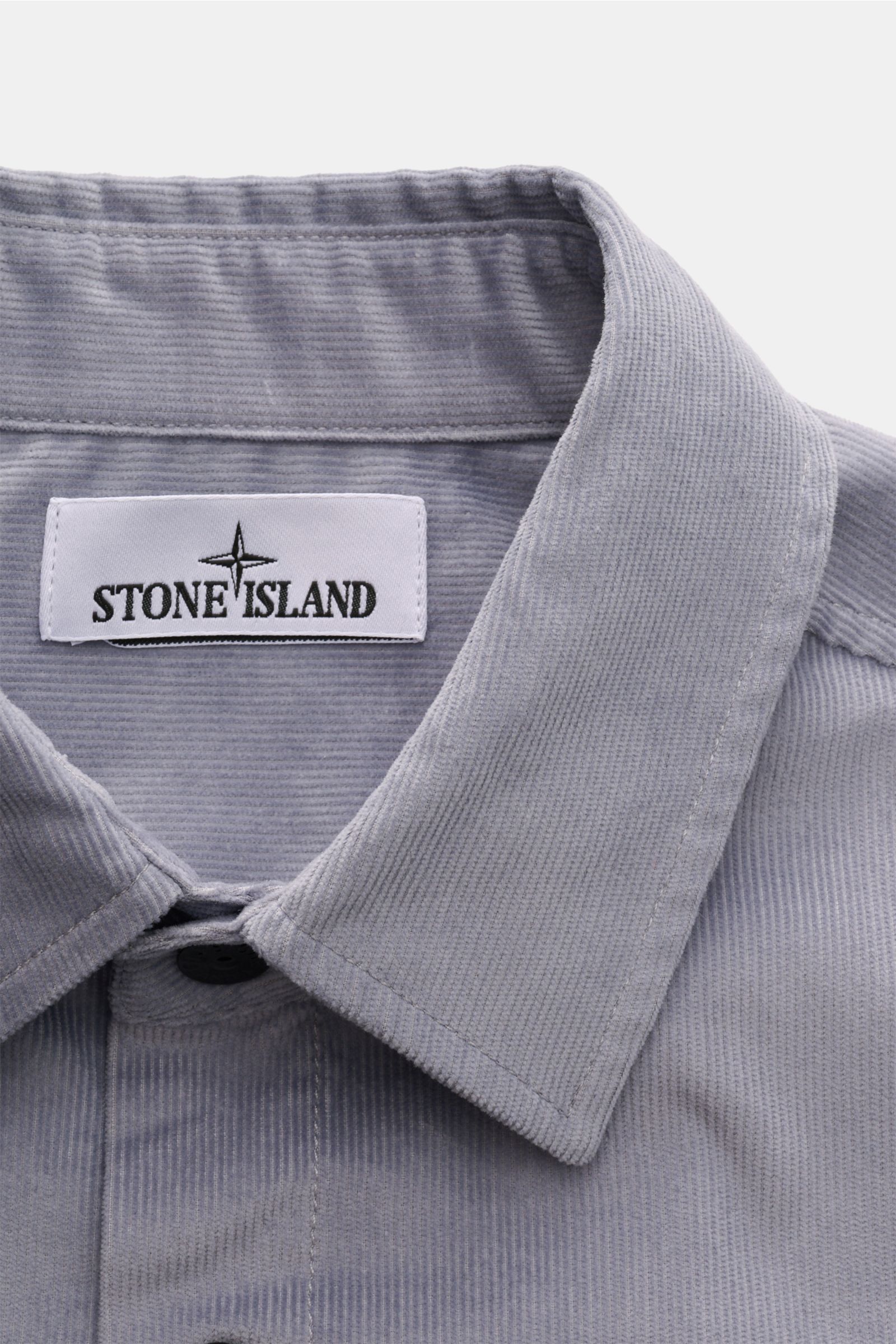 Nahaufnahme des Stone Island Cord Overshirts rauchblau von oben, zeigt Umlegekragen, weichen Bio-Baumwoll-Cord und Markenlabel innen.