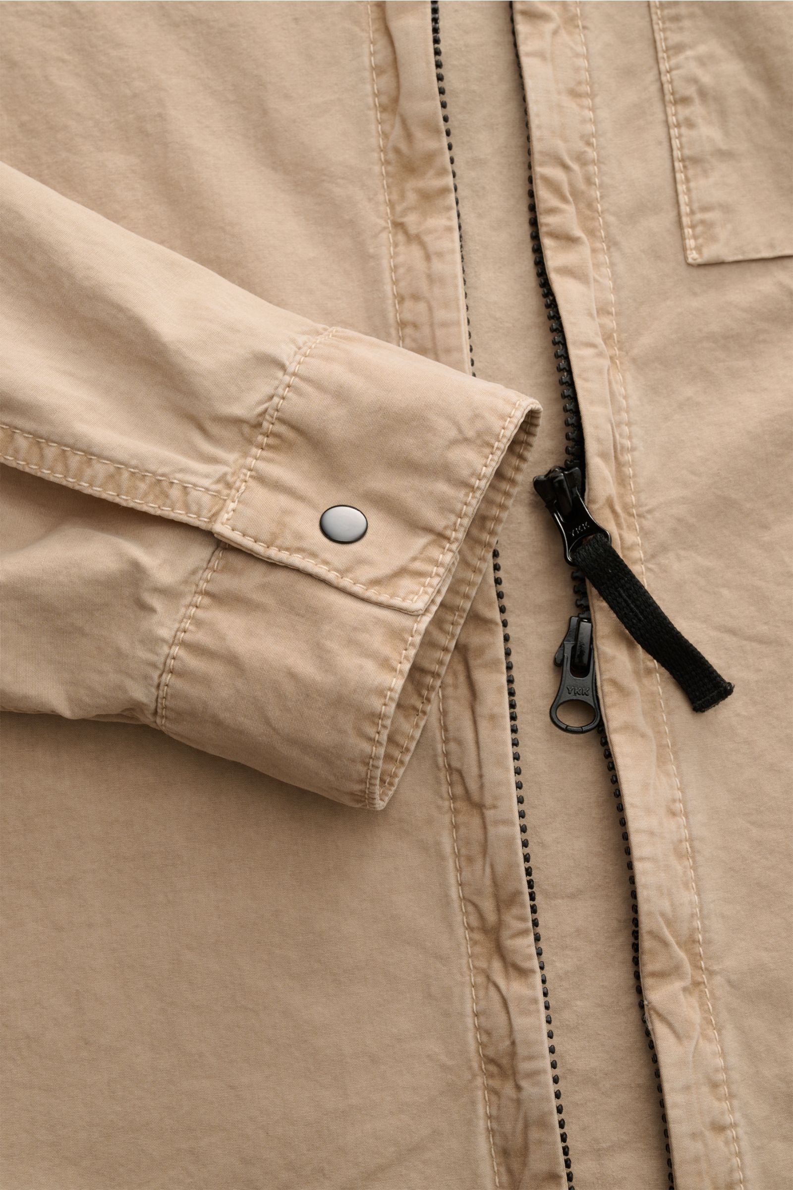Nahaufnahme des Stone Island Overshirt 'Brushed Canvas' beige, Slim Fit aus reiner Baumwolle mit Zwei-Wege-Reißverschluss, Knopfärmelabschluss und Brusttasche.