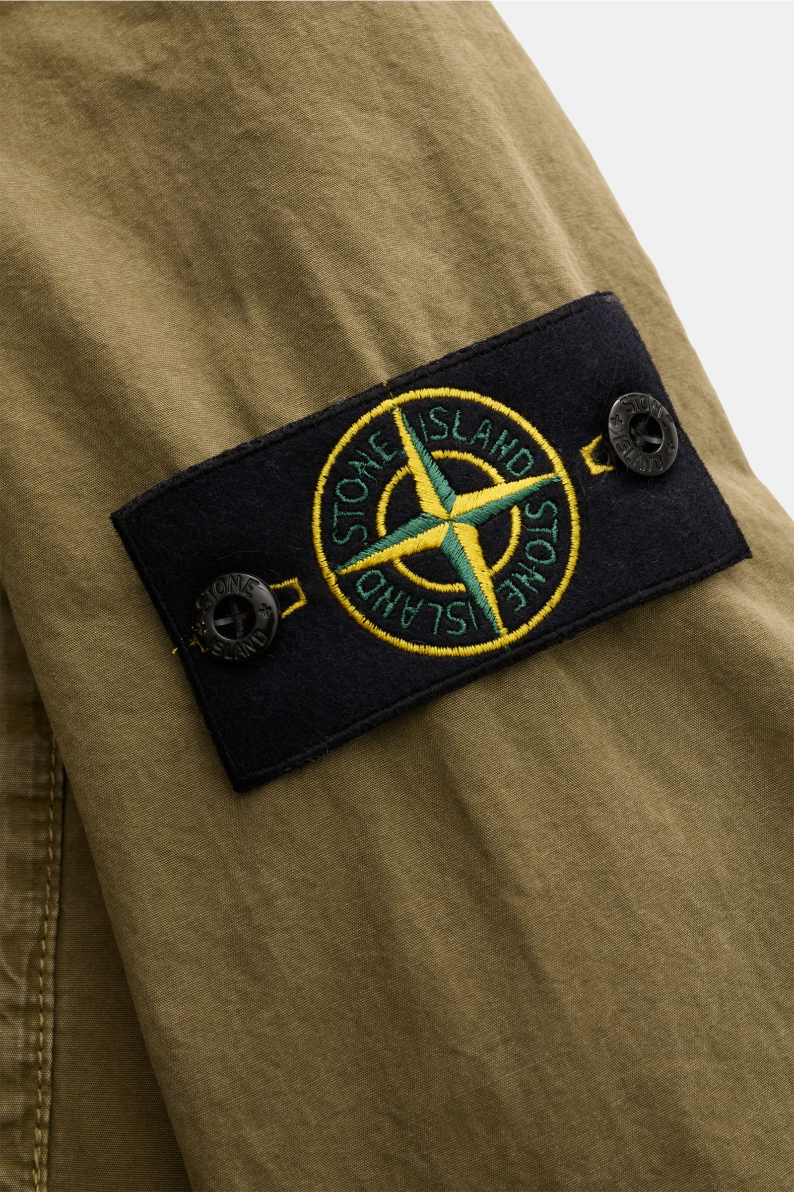 Stone Island Overshirt 'Brushed Canvas' oliv, Detailansicht des Kompass-Badges am Ärmel aus reiner Baumwolle mit weichem Griff.