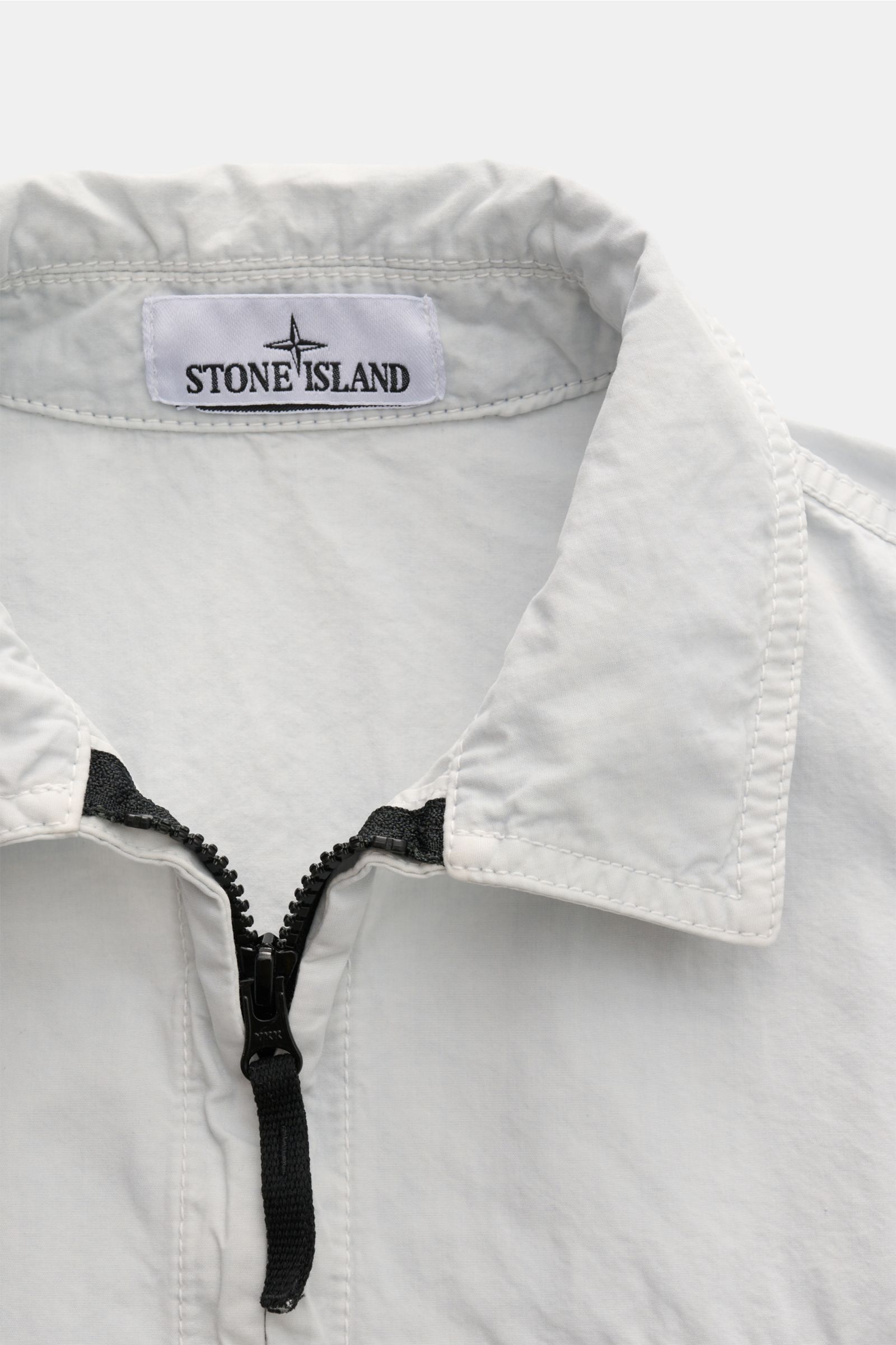 Nahaufnahme des Stone Island Overshirt 'Brushed Canvas' pastellblau mit Umlegekragen und zwei-Wege-Reißverschluss aus reiner Baumwolle.
