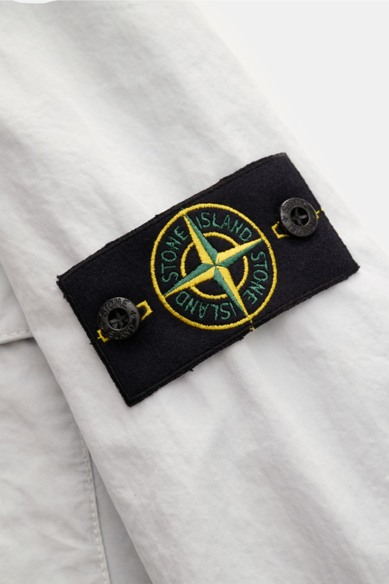 Stone Island Overshirt 'Brushed Canvas' pastellblau, Nahaufnahme vom Ärmel mit schwarzem Kompass-Badge, reine Baumwolle, Slim Fit.