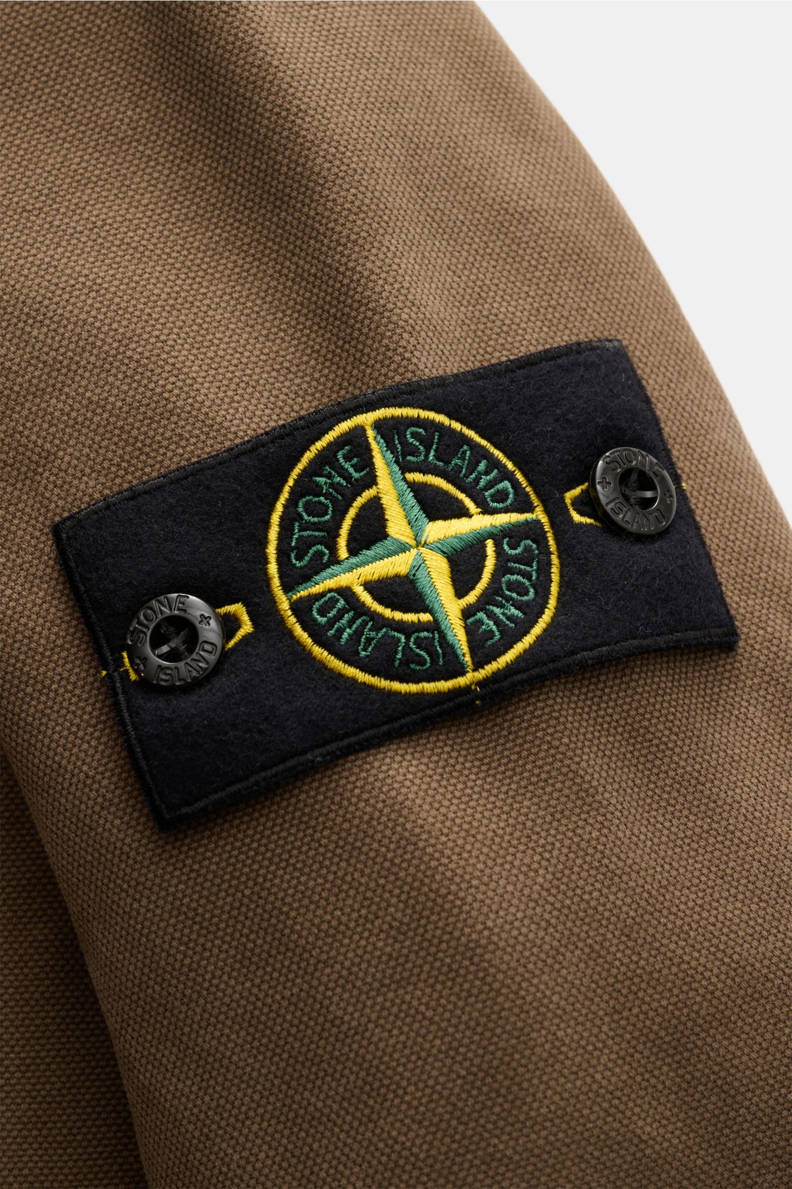 Close-up front view of Stone Island Overshirt 'Panama' khaki fabric showcasing the black compass badge on the sleeve, made of pure cotton with a soft touch, slim fit, sturdy two-way zipper, stand-up collar, chest pocket, buttoned cuffs, and versatile laye
