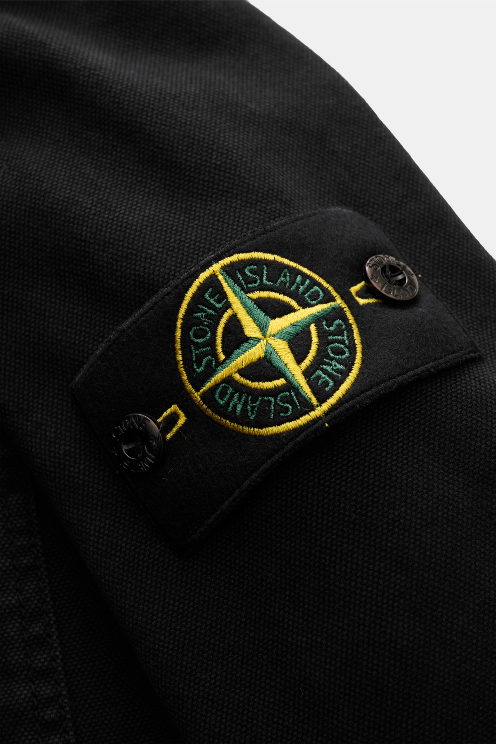 Nahaufnahme des Kompass-Badges am Ärmel des Stone Island Overshirt 'Panama' schwarz aus reiner Baumwolle mit robustem Zwei-Wege-Reißverschluss.