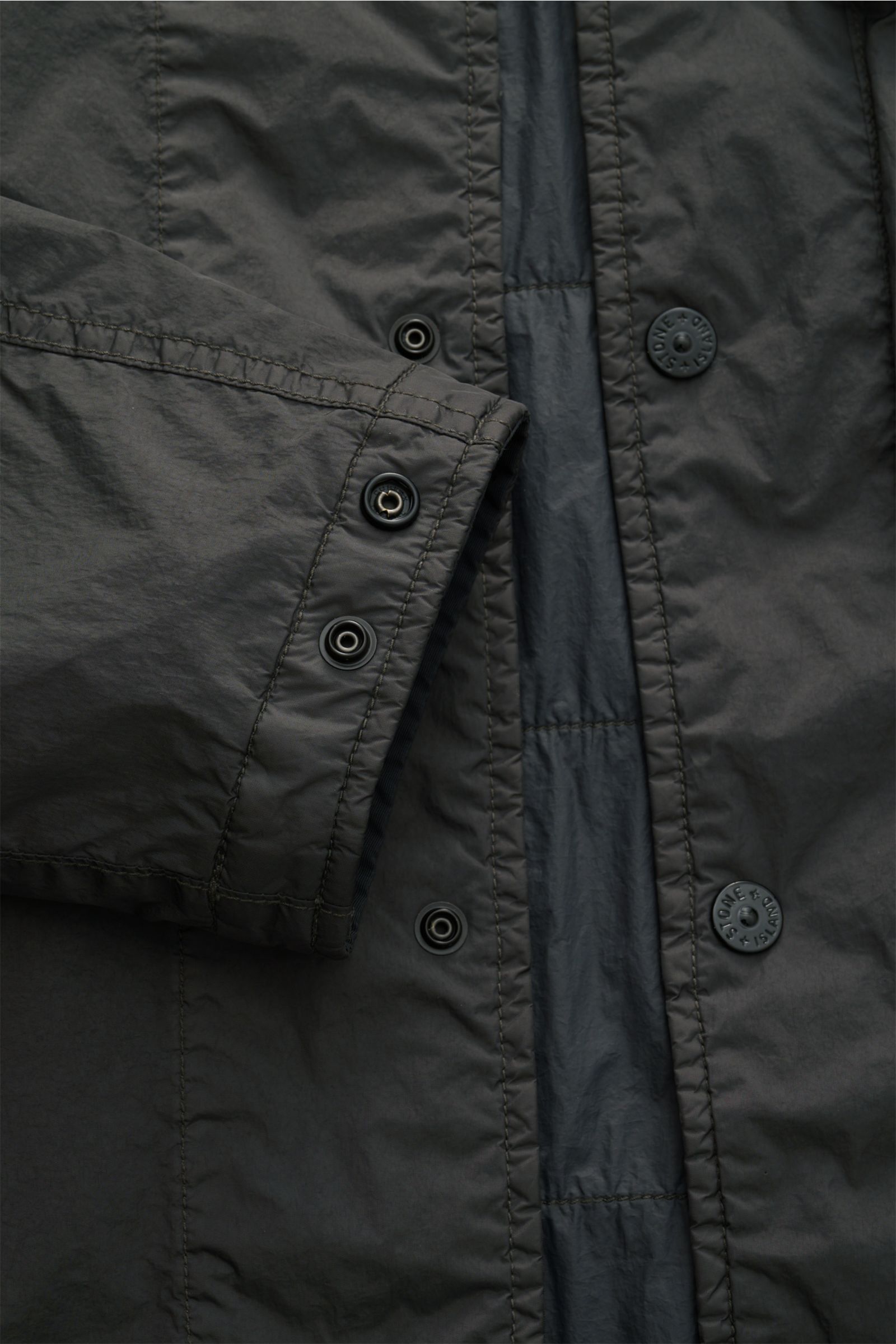 Close-up top-down view of the Stone Island Overshirt 'Crinkle Reps' dunkelgrau in dark grey, showing snap button placket and sleeve cuff details.

Additional description: 
Funktion trifft urbanen Style: Eine ultraleichte Konstruktion aus wind- und wass