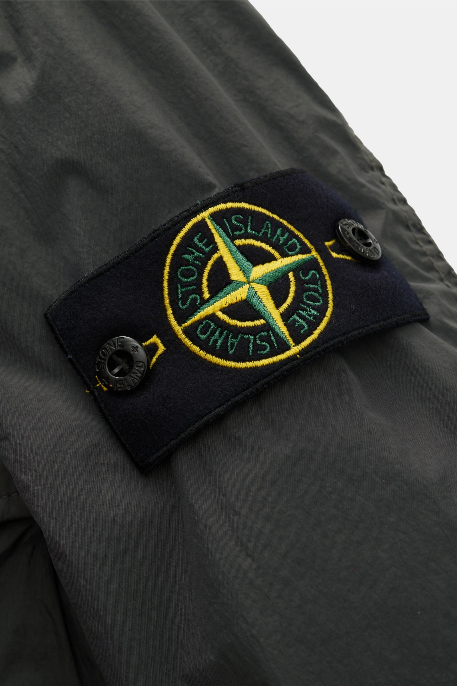 Close-up front-side view of the Stone Island Overshirt 'Crinkle Reps' dunkelgrau showing the typical compass badge on dark gray, wind- and water-repellent microfiber fabric, featuring slim fit, garment dyed design, snap button placket, spread collar, ches