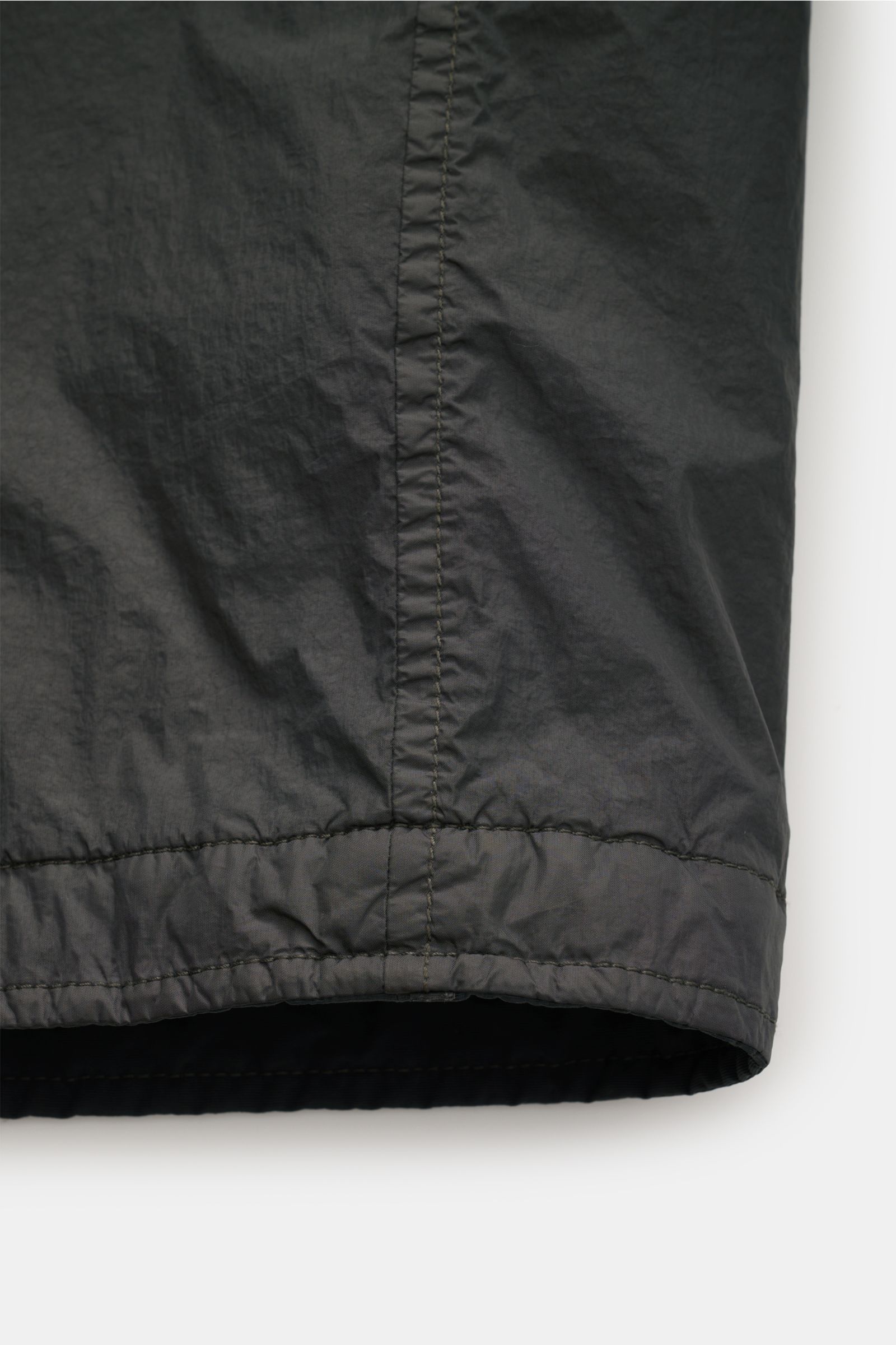 Close-up of the lower hem of the Stone Island Overshirt 'Crinkle Reps' dunkelgrau, showing the wind- and water-resistant microfiber fabric with garment-dyed design, photographed from the front bottom perspective.

Description: Funktion trifft urbanen Styl
