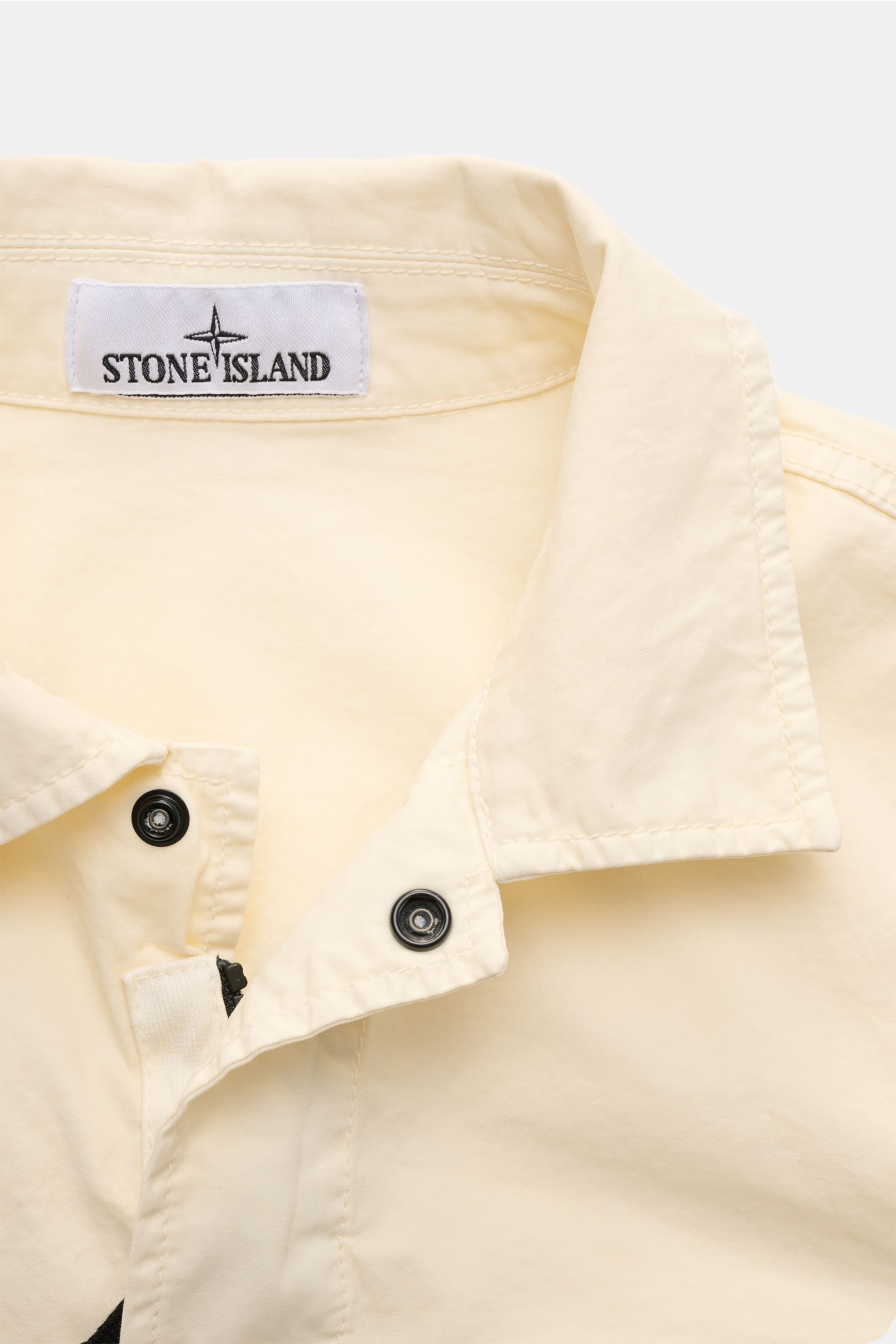 Close-up front view of Stone Island Overshirt 'Stretch Cotton' creme collar and upper chest, showing garment-dyed, soft, slightly stretchy pure cotton fabric with snap buttons and Stone Island label.

Description: Sportives Overshirt mit urbaner Lässig