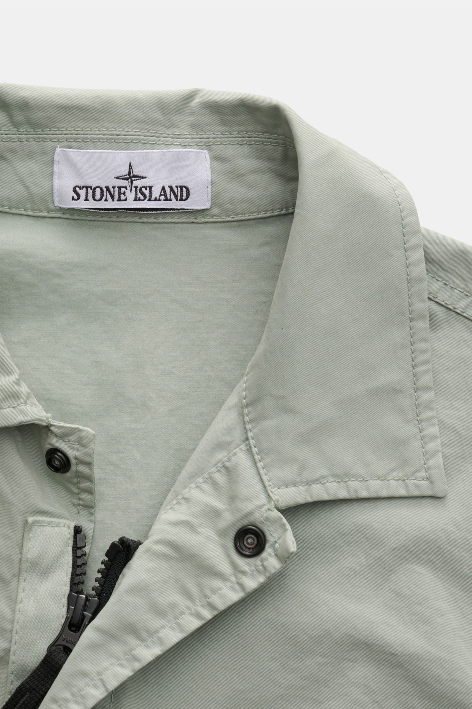 Close-up front top view of Stone Island Overshirt 'Stretch Cotton' salbei in soft sage green, showing elastic cotton fabric, slim fit, collar, zipper, and snap button details.

Description: Sportives Overshirt mit urbaner Lässigkeit: Dieser markante Hy