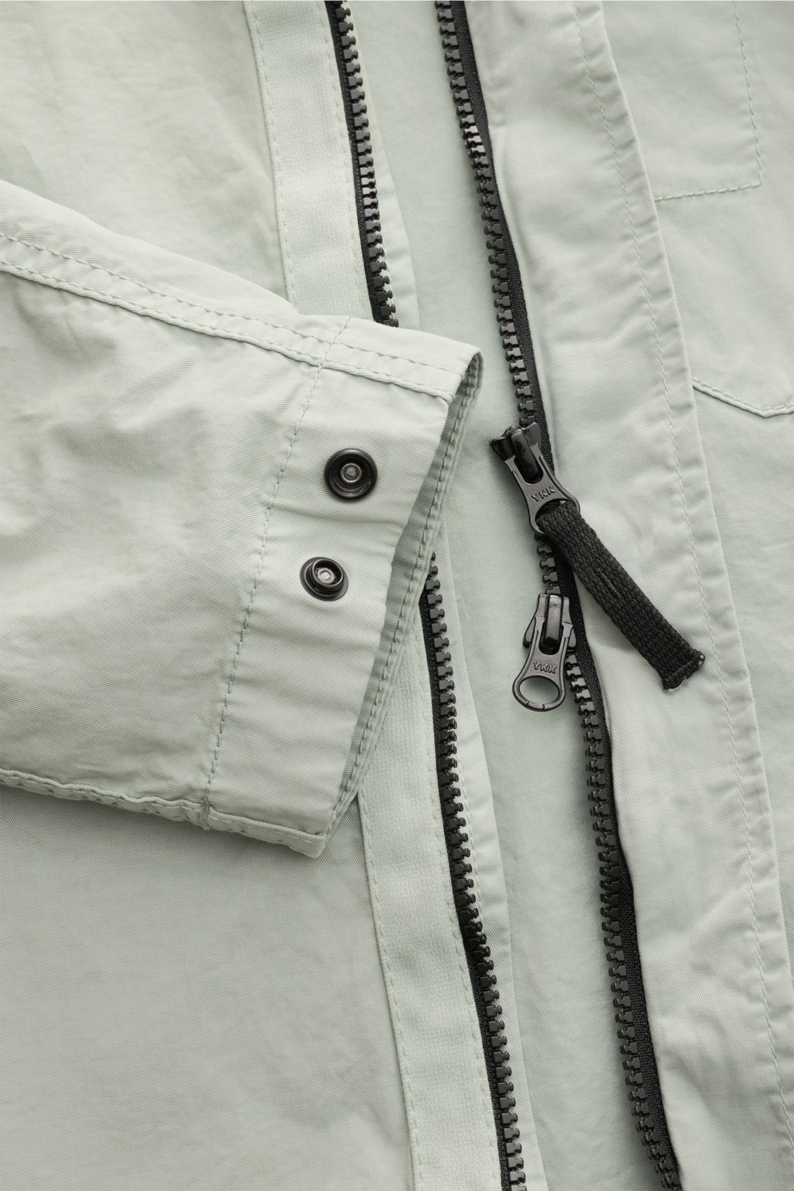 Close-up front view of Stone Island Overshirt 'Stretch Cotton' salbei showing elastic cotton fabric, soft touch, slim fit, two-way zipper, snap-button cuffs, and stitching details. Sportives Overshirt mit urbaner Lässigkeit: Dieser markante Hybrid aus Cas
