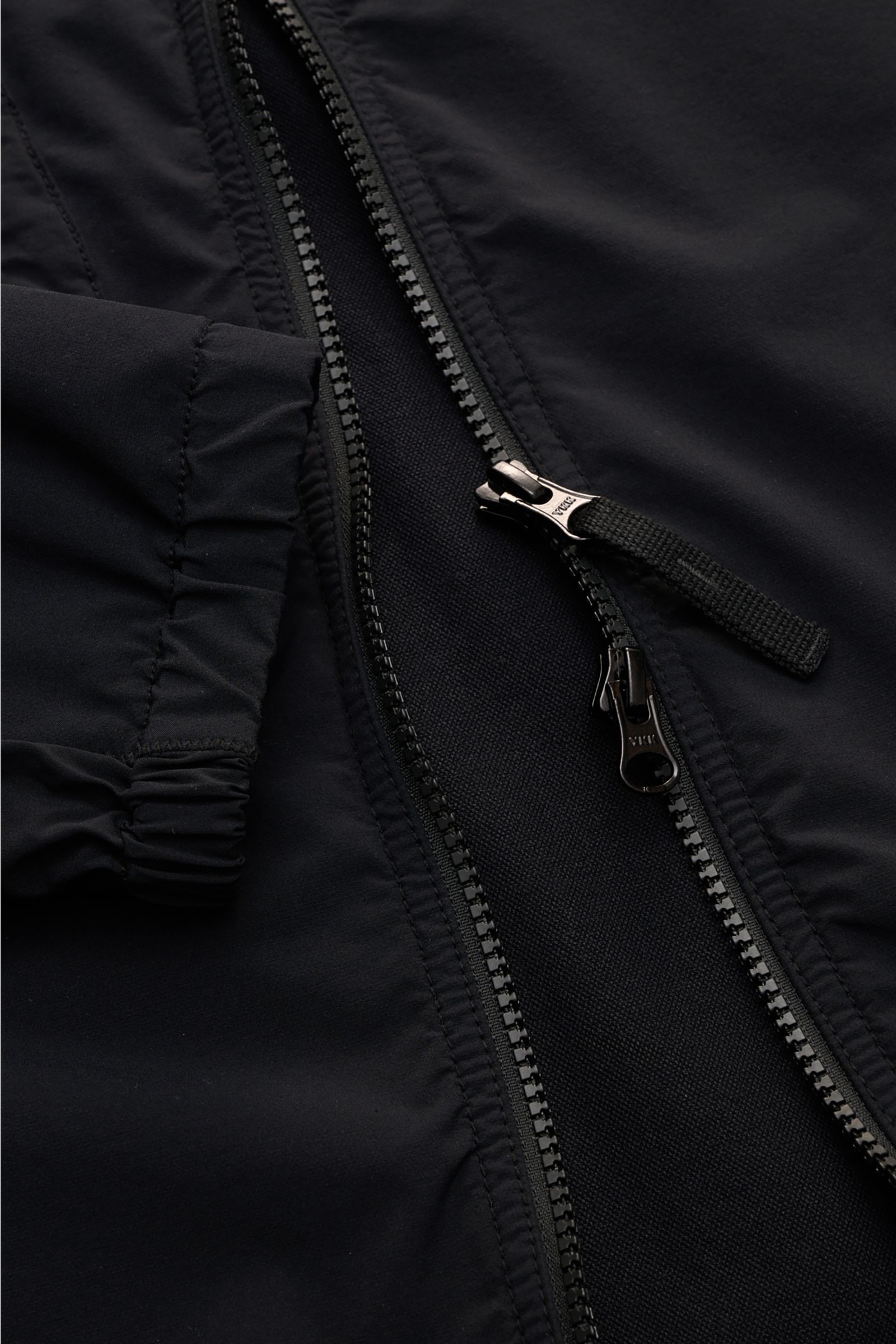 Close-up image of the Stone Island Overshirt 'Nylon Stretch' black showing the smooth, stretchy microfibre fabric, robust two-way black zipper, and elasticated cuff from a top-down perspective. Function and comfort by STONE ISLAND: The overshirt 'Nylon St