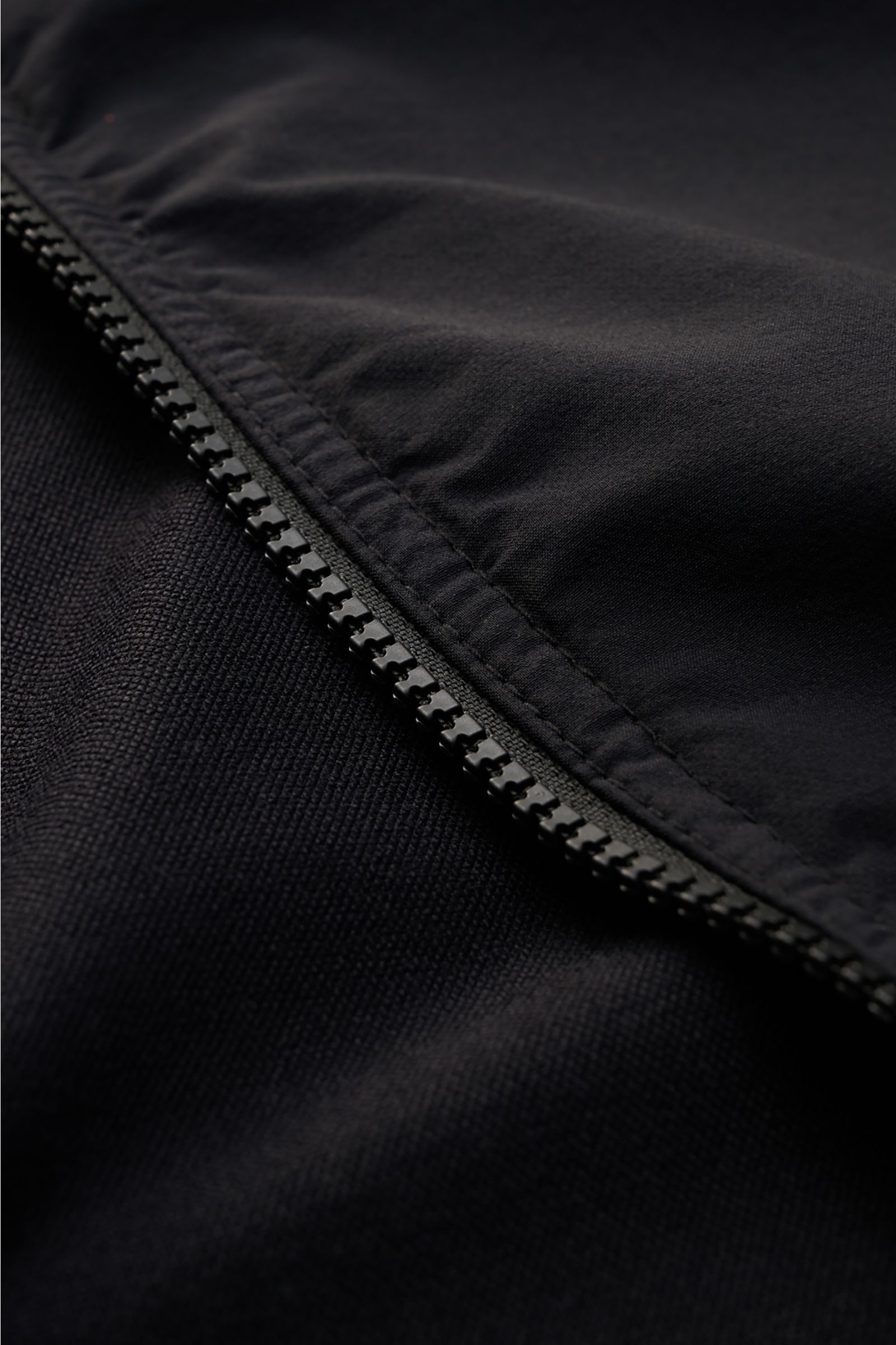 Close-up view of the robust two-way zip on the Stone Island Overshirt 'Nylon Stretch' black, showing smooth, stretchy microfibre fabric. Function and comfort by STONE ISLAND: The overshirt 'Nylon Stretch' is made of stretchy microfibre which makes it an i