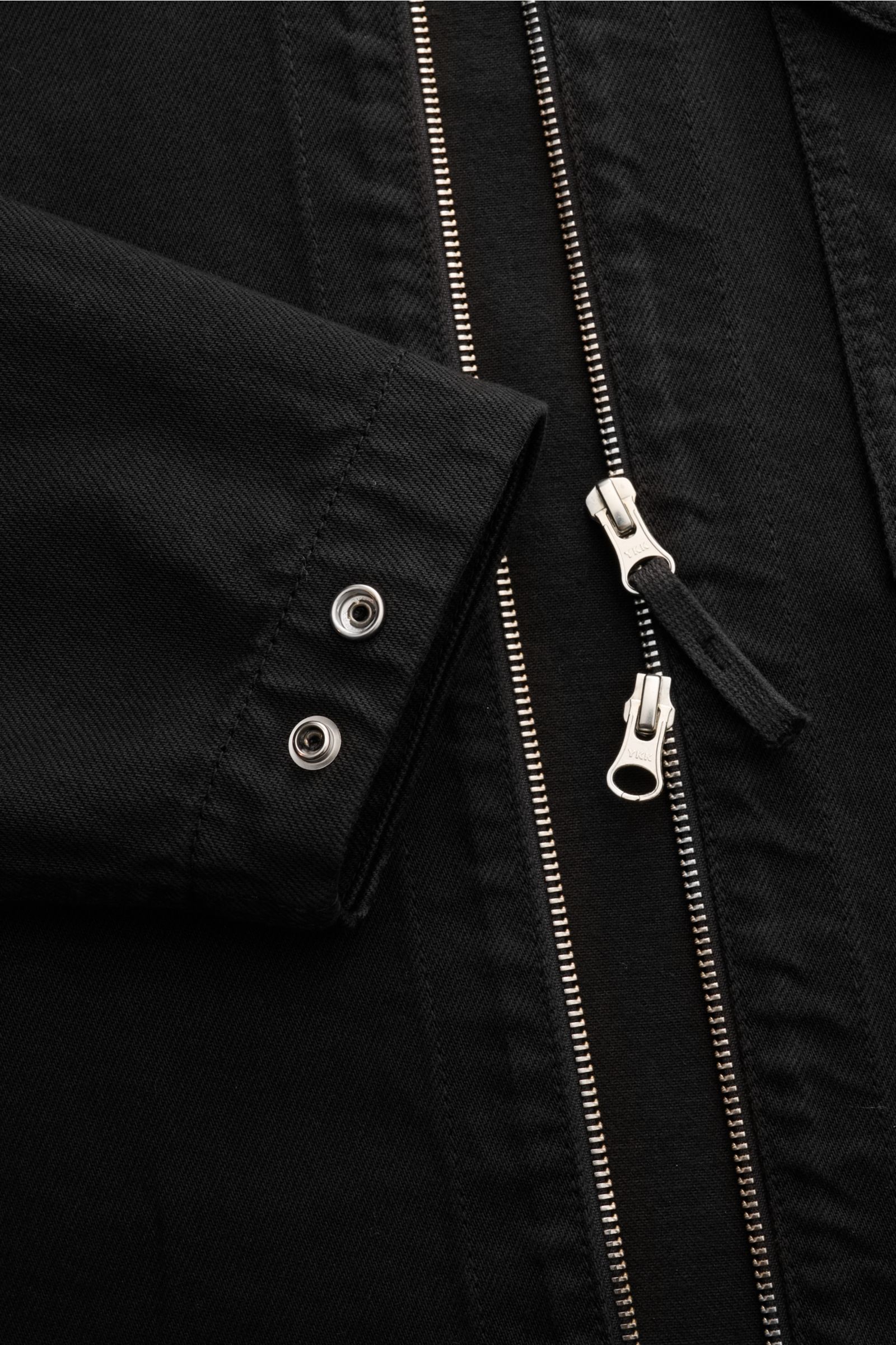 Nahaufnahme des Stone Island Jeans-Overshirt schwarz von schräg oben, zeigt Ärmelabschluss mit Druckknöpfen und zwei-Wege-Reißverschluss.