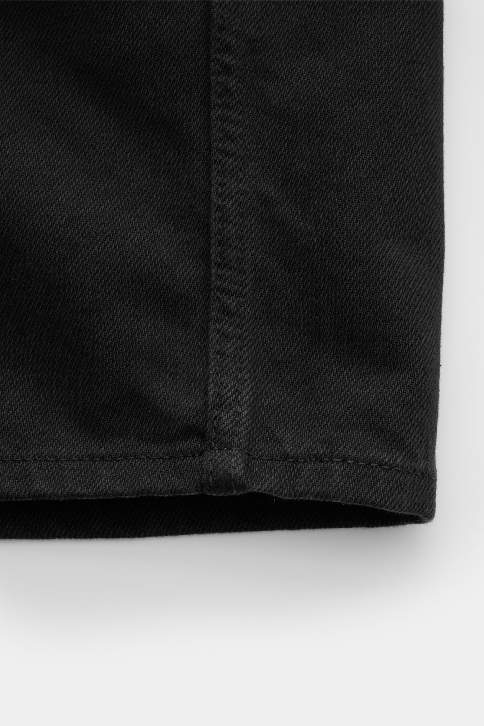 Nahaufnahme des unteren Saums des Stone Island Jeans-Overshirt schwarz aus robustem Bull Denim in Slim Fit mit typischer Struktur, fotografiert von vorne unten.
