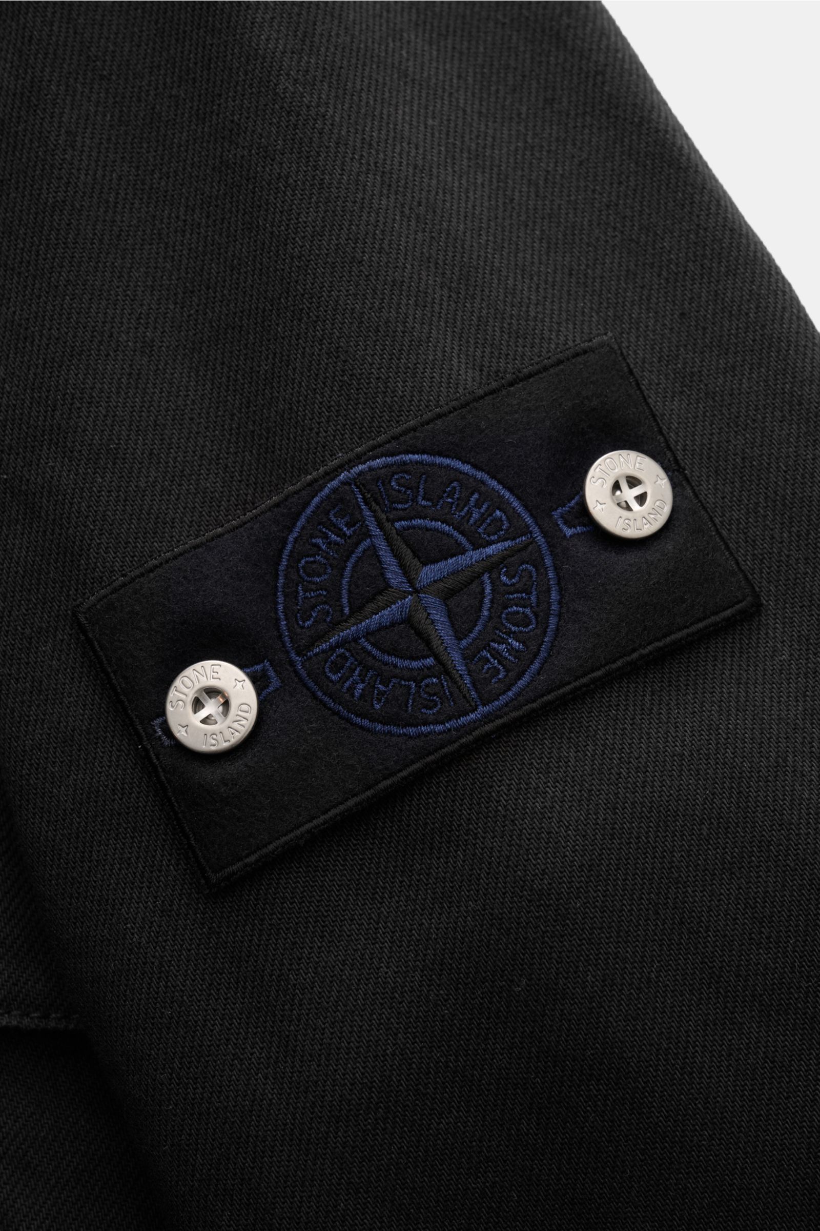 Stone Island Jeans-Overshirt schwarz, Nahaufnahme Kompass-Badge am Ärmel aus robustem Baumwoll-Denim mit markanter Struktur.