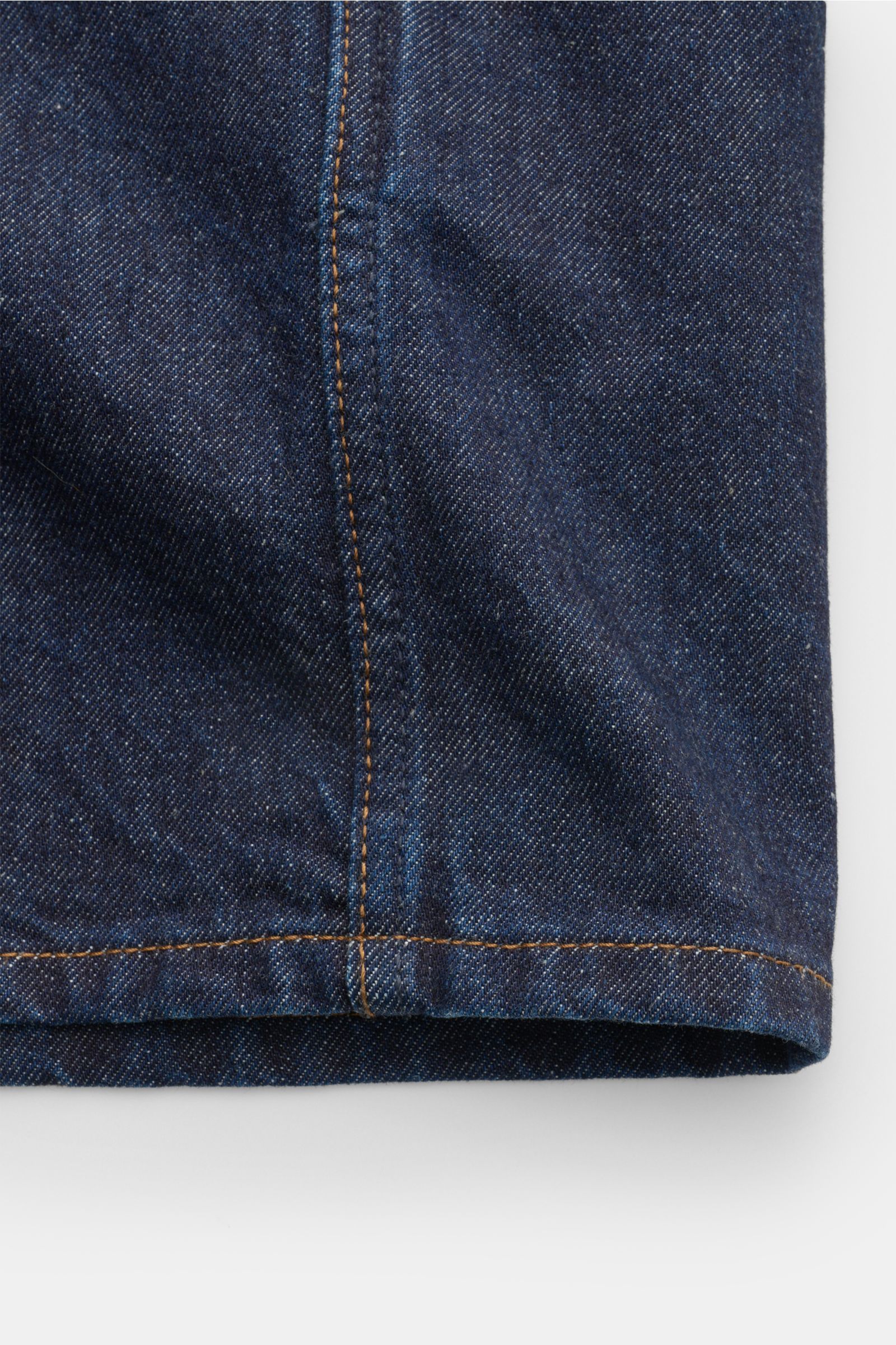 Close-up side view of the slightly rounded hem and vertical seam of the Stone Island Denim overshirt navy, made from indigo-dyed pure cotton denim with typical fabric texture. For casual denim looks: Made from indigo-dyed cotton yarn, this overshirt from 