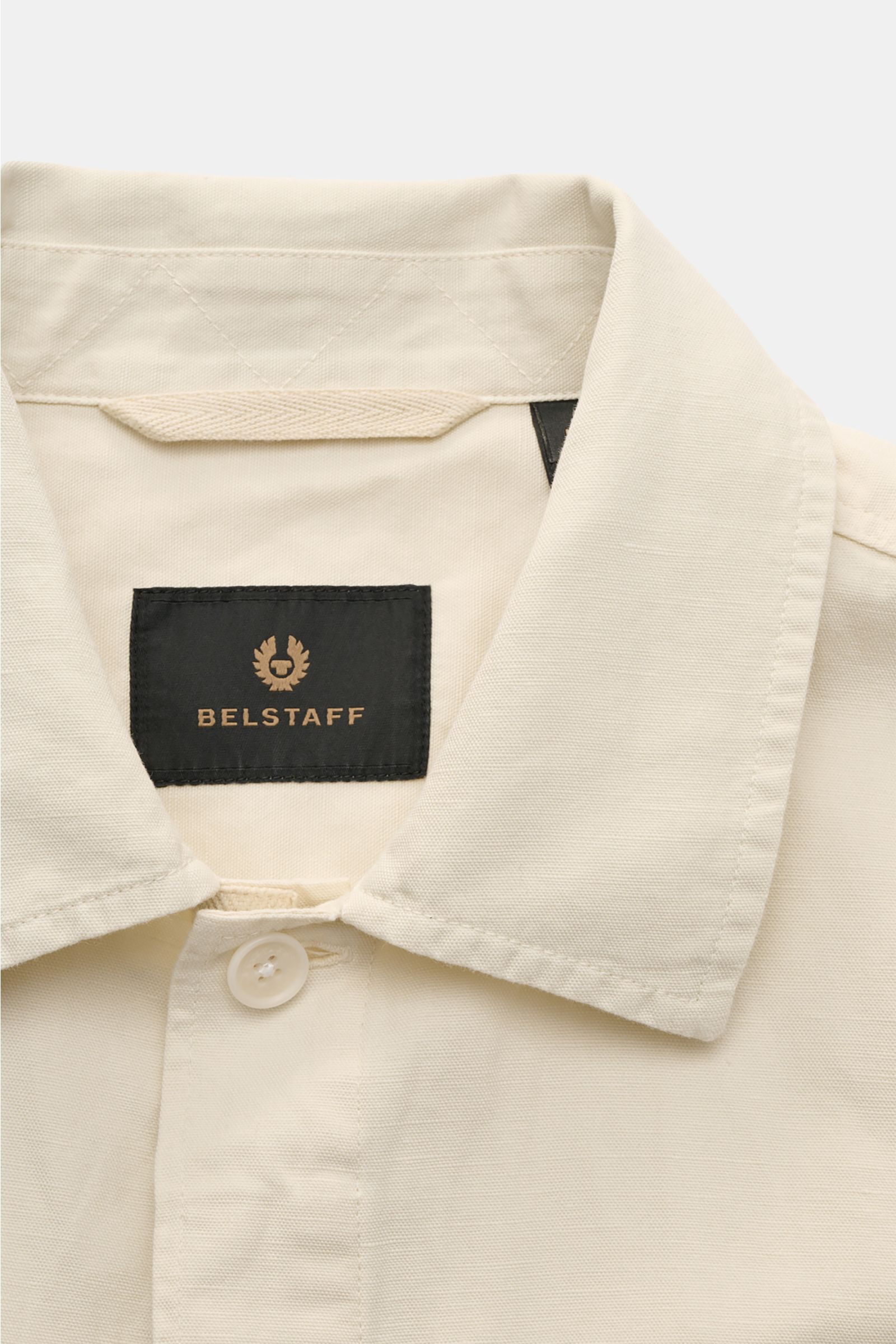 Close-up front view of Belstaff Overshirt 'Maritime' sand showing narrow collar, concealed button placket, and black Belstaff label inside collar in a cotton-linen blend with slim fit and classic details.