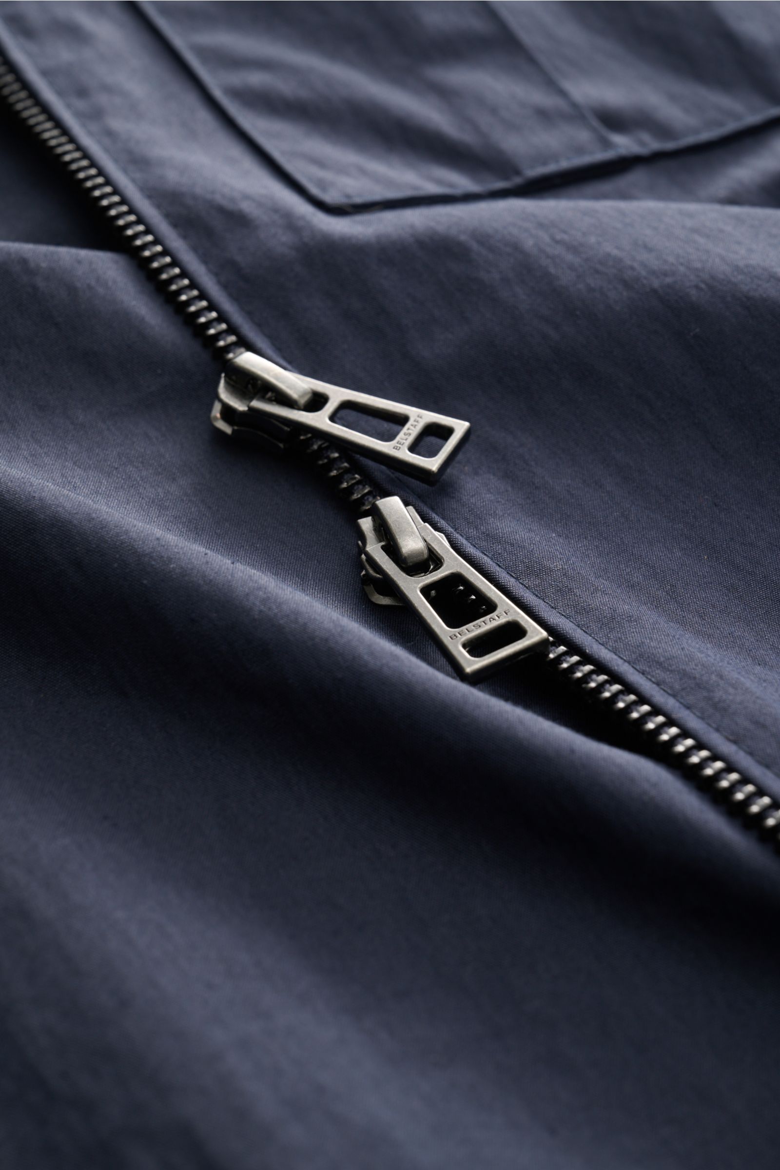 Nahaufnahme des zweifarbigen Zwei-Wege-Reißverschlusses mit BELSTAFF-Prägung am Belstaff Overshirt 'Cargo' navy aus Baumwoll-Microfaser-Mix.