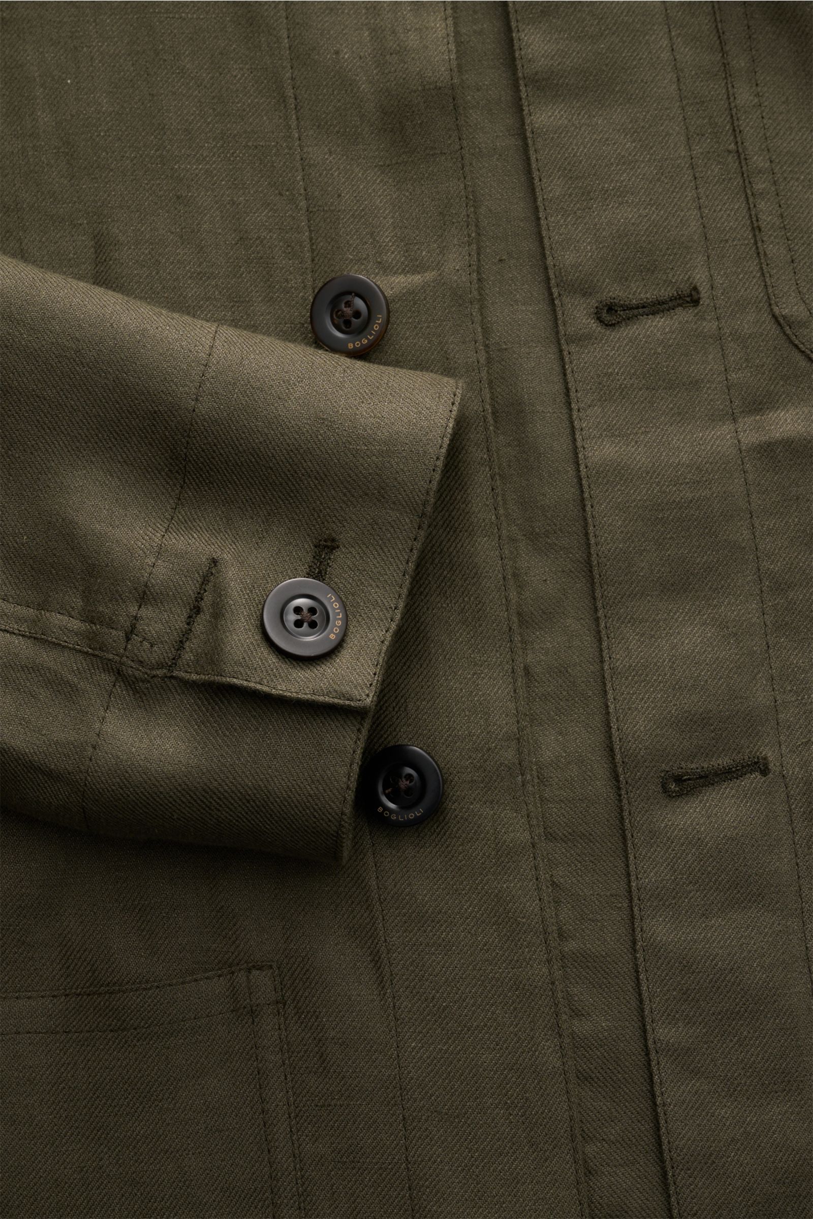 Nahaufnahme des Boglioli Leinen Overshirt oliv von oben, zeigt feinen Twill, Knopfleiste, Ärmel mit Knopf und aufgesetzte Taschen.